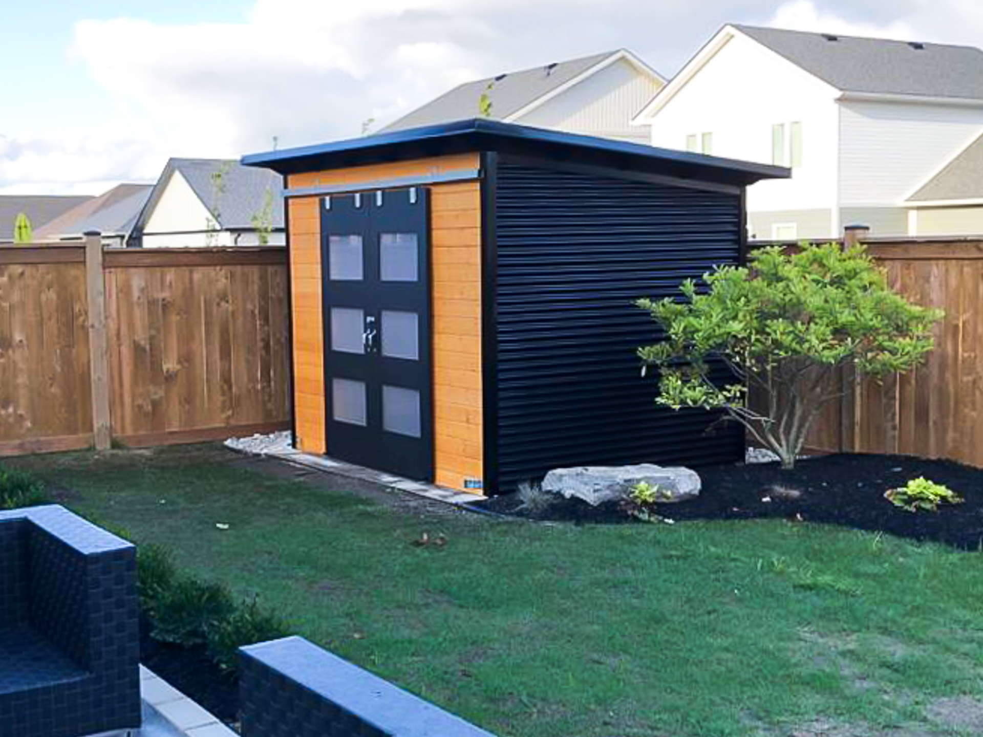 Side angle of 10x8 Essential Shed showing black corrugated steel siding and cedar stain pine front wall with sliding barn doors in St. Thomas Ontario, built by Backyard Escape Studios.