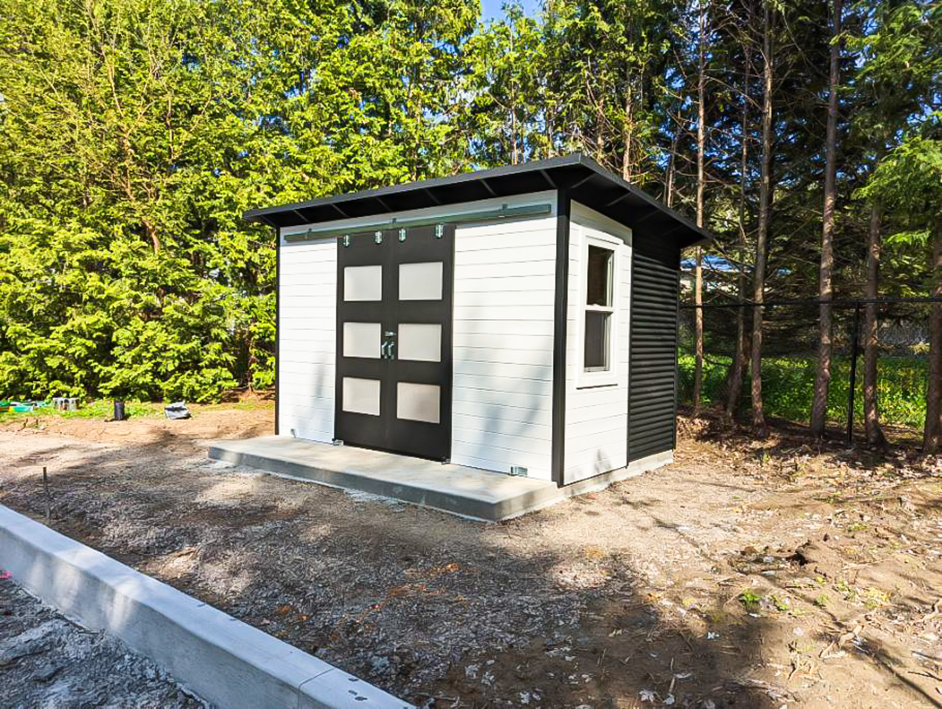 13x8 Essential Shed in Ancaster Ontario with White Satin pine T+G siding and Jet Black corrugated steel, double sliding barn doors with frosted glass panels and single-hung side window, installed by Backyard Escape Studios.