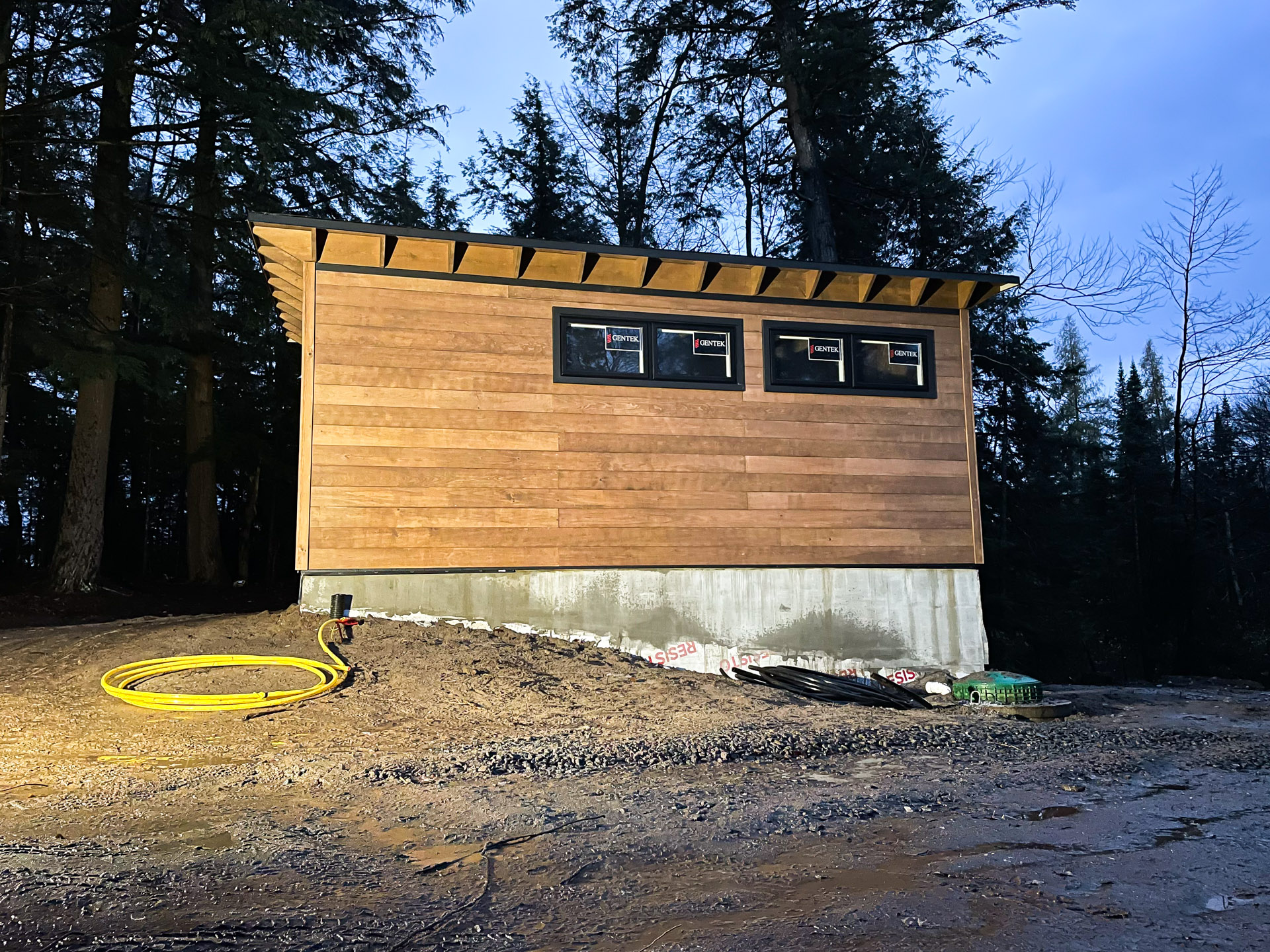 22x16 Advanced Studio front view with horizontal cedar siding, full-height glass entry doors, and decorative rafter-tail roofline on a wooded Oakville Ontario property, installed by Backyard Escape Studios.