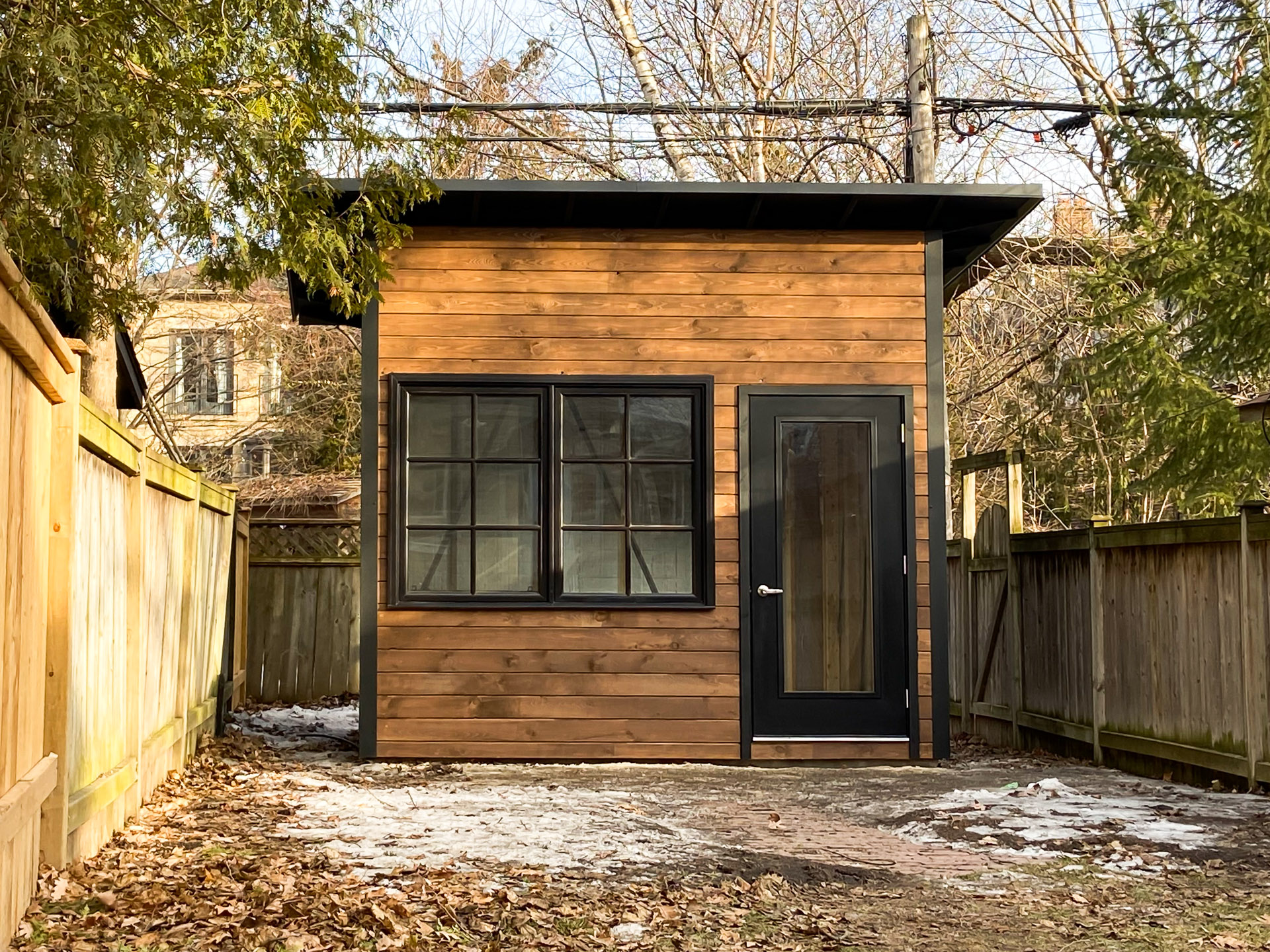 11x9 Advanced Studio with horizontal cedar pine front wall in Muskoka Brown, jet black corrugated steel siding, full glass outswing door, and black offset window in Toronto Ontario, installed by Backyard Escape Studios.