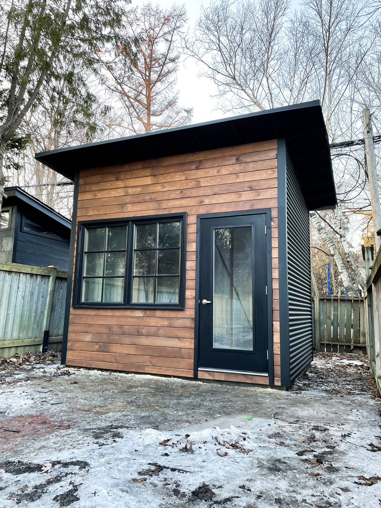 Side view of 11x9 Advanced Studio with jet black corrugated steel siding and black mono-slope roof overhang in Toronto Ontario, installed by Backyard Escape Studios.