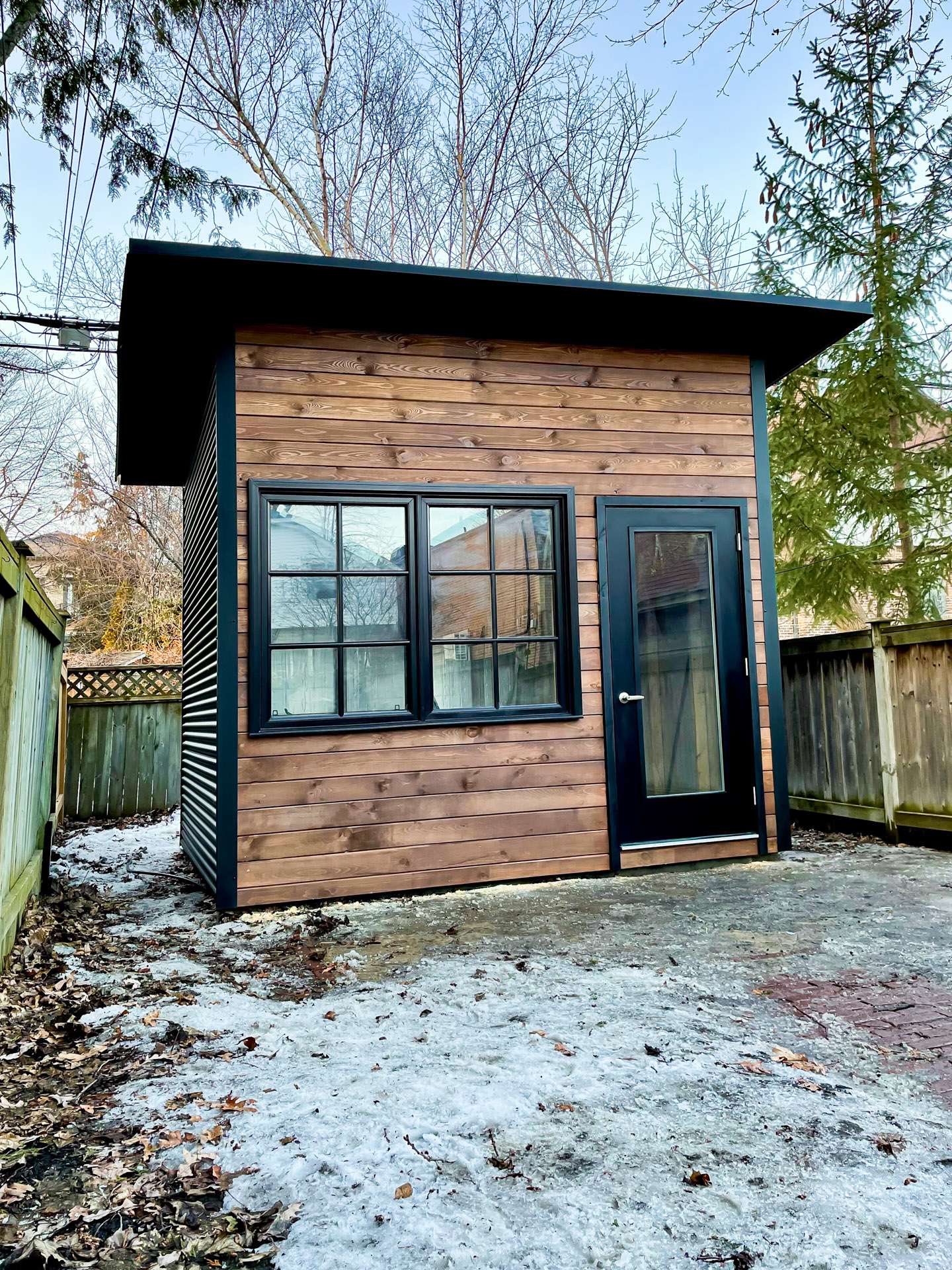 Front-left angle of 11x9 Advanced Studio showing cedar pine front wall and jet black corrugated steel siding with mono-slope roof in Toronto Ontario, installed by Backyard Escape Studios.