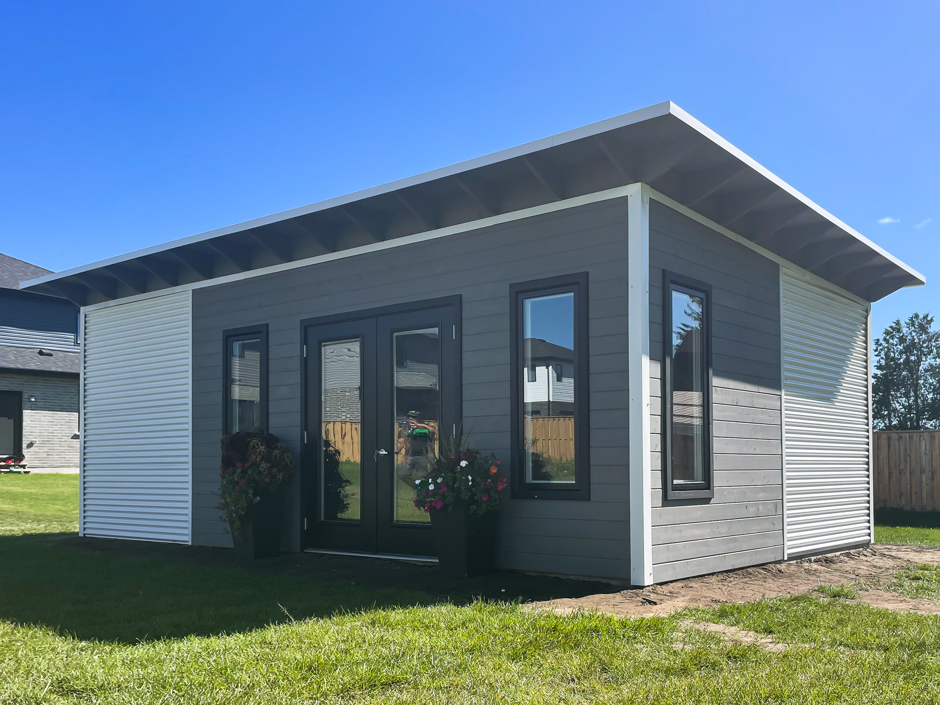 Close-up of Advanced Shed studio front wall with full-glass French doors, three tall fixed-pane windows, and Kendall Charcoal stained pine T&G in Mount Brydges Ontario, installed by Backyard Escape Studios.