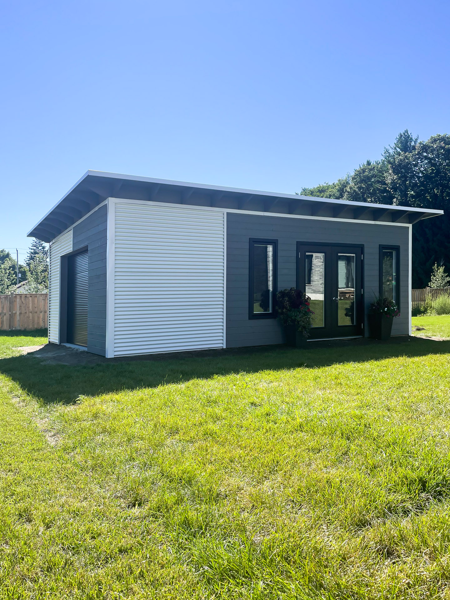 Full view of 25x15 Advanced Shed backyard studio with monoslope roof, Cambridge White steel siding and Kendall Charcoal pine front in Mount Brydges Ontario, installed by Backyard Escape Studios.