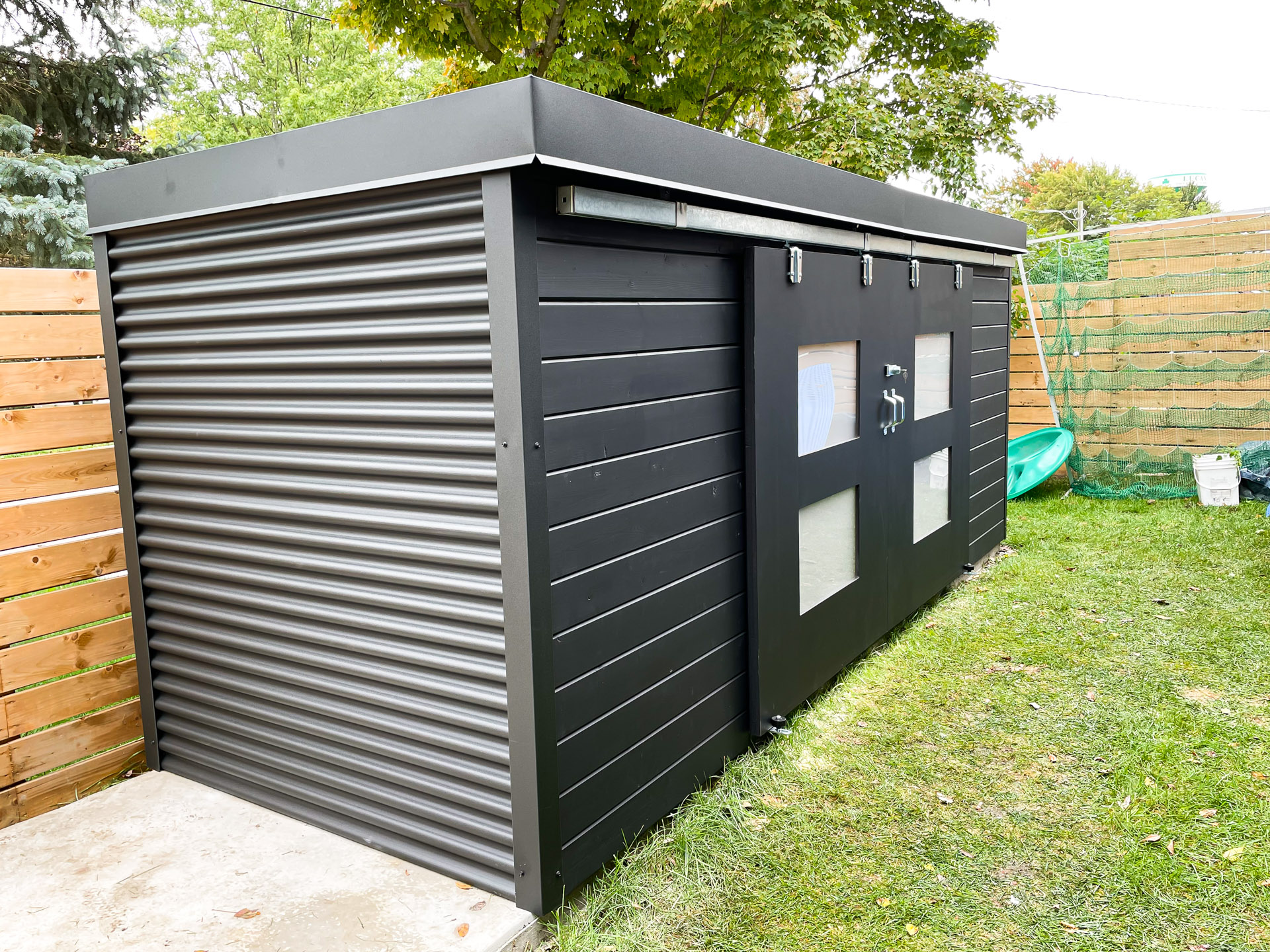 15x5 Cube Shed with Jet Black corrugated steel siding, Black Beauty stained pine front wall, and custom double sliding barn doors with frosted glass windows in Lucan Ontario, installed by Backyard Escape Studios.