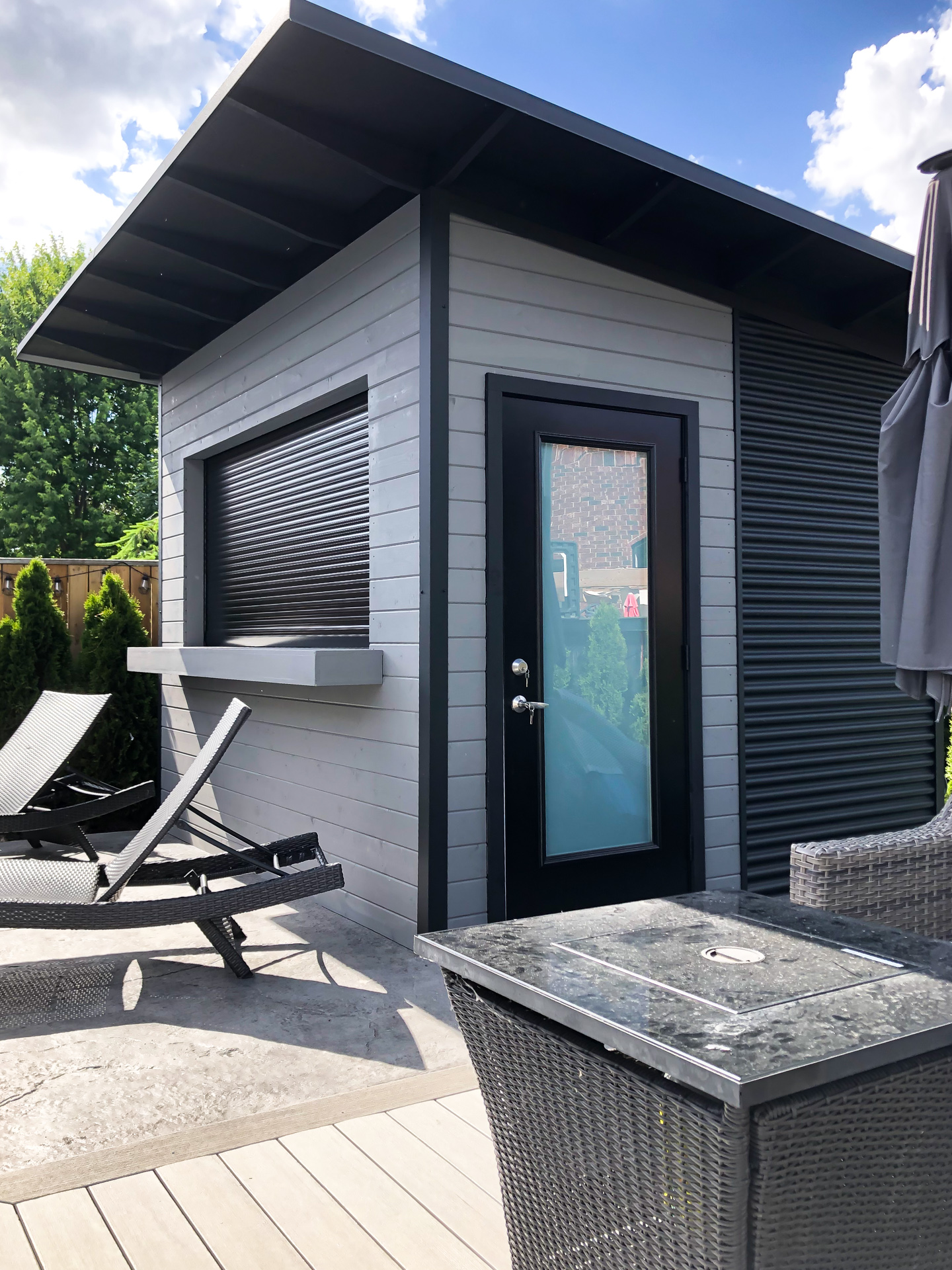 Corner view of 11x9.5 Advanced pool shed in London Ontario showing frosted glass outswing door, roll-up bar window, and pine T+G siding in Kendall Charcoal, installed by Backyard Escape Studios.
