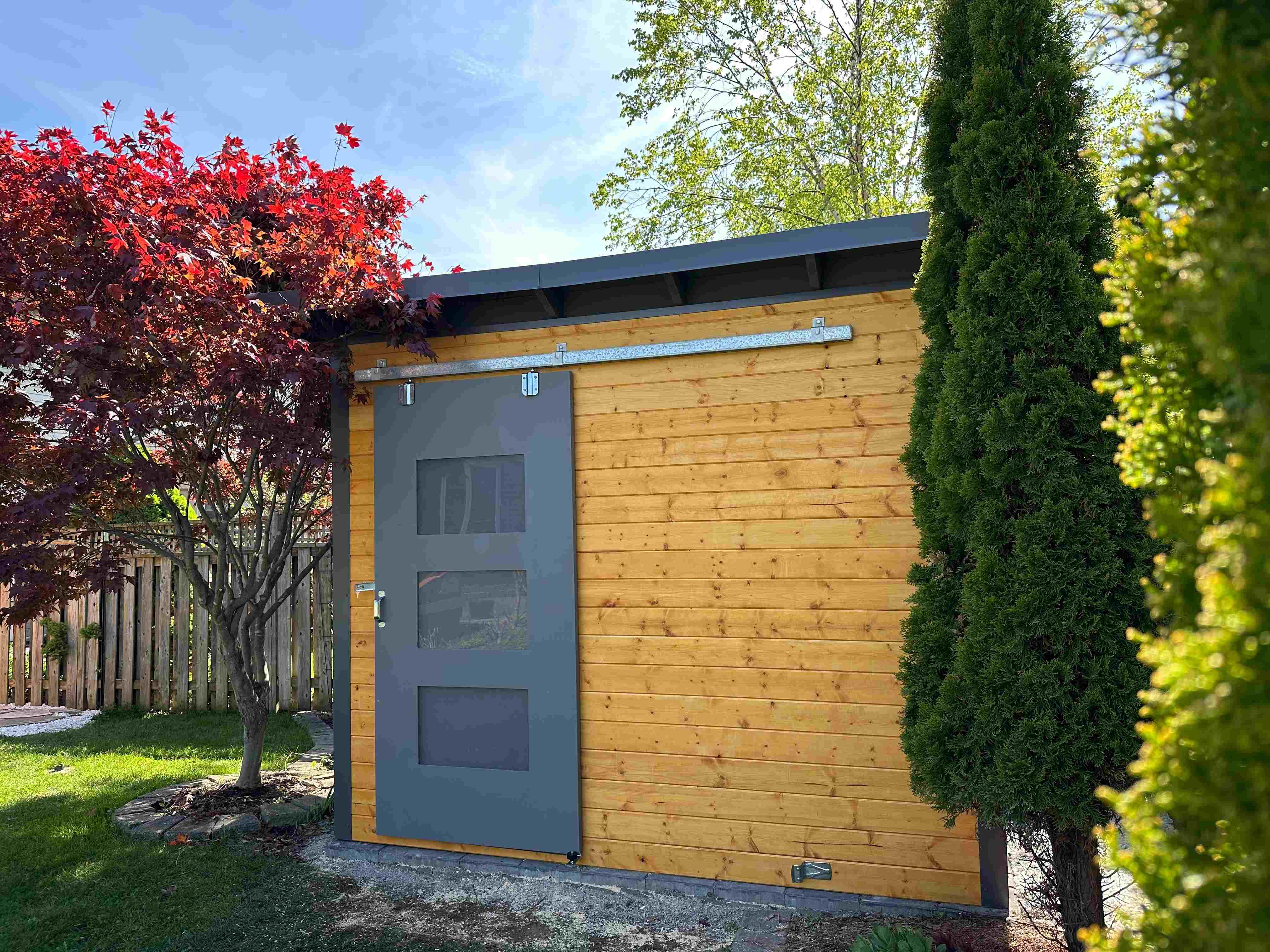 10x8 Essential Shed with cedar stain pine front wall, charcoal corrugated steel siding, and black sliding barn door in London Ontario, installed by Backyard Escape Studios.