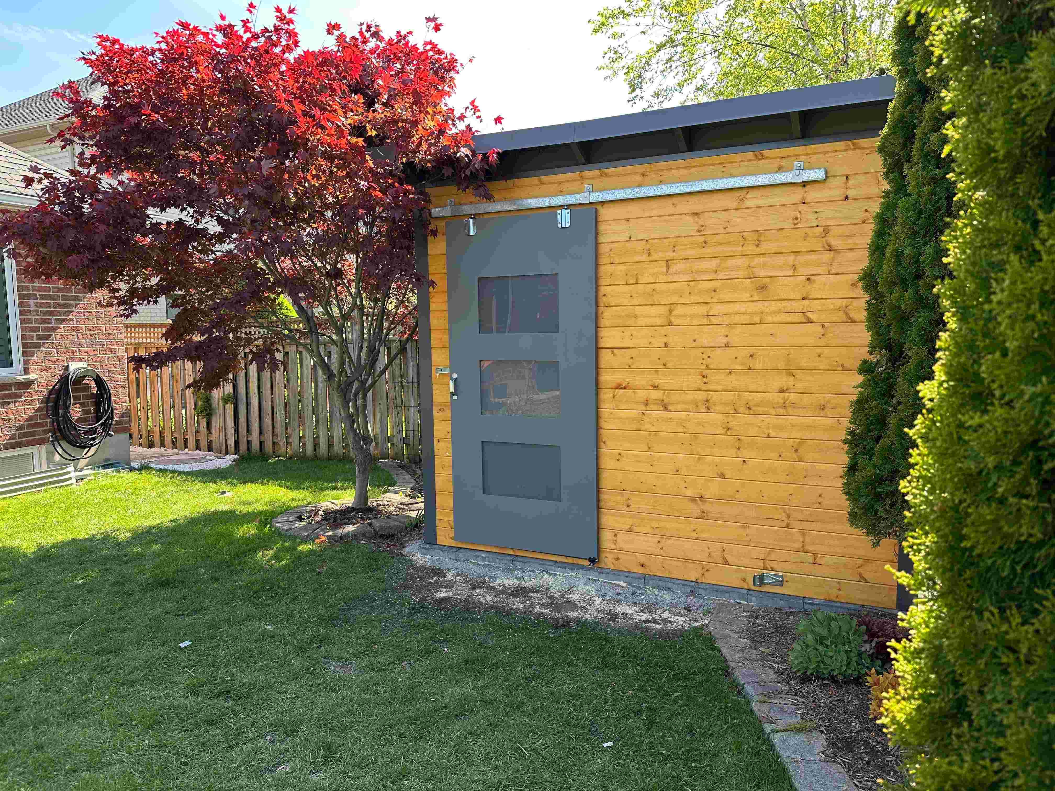 Finished 10x8 Essential Shed in London Ontario with Black Beauty sliding barn door, cedar stain pine front wall, and charcoal corrugated steel siding installed by Backyard Escape Studios.