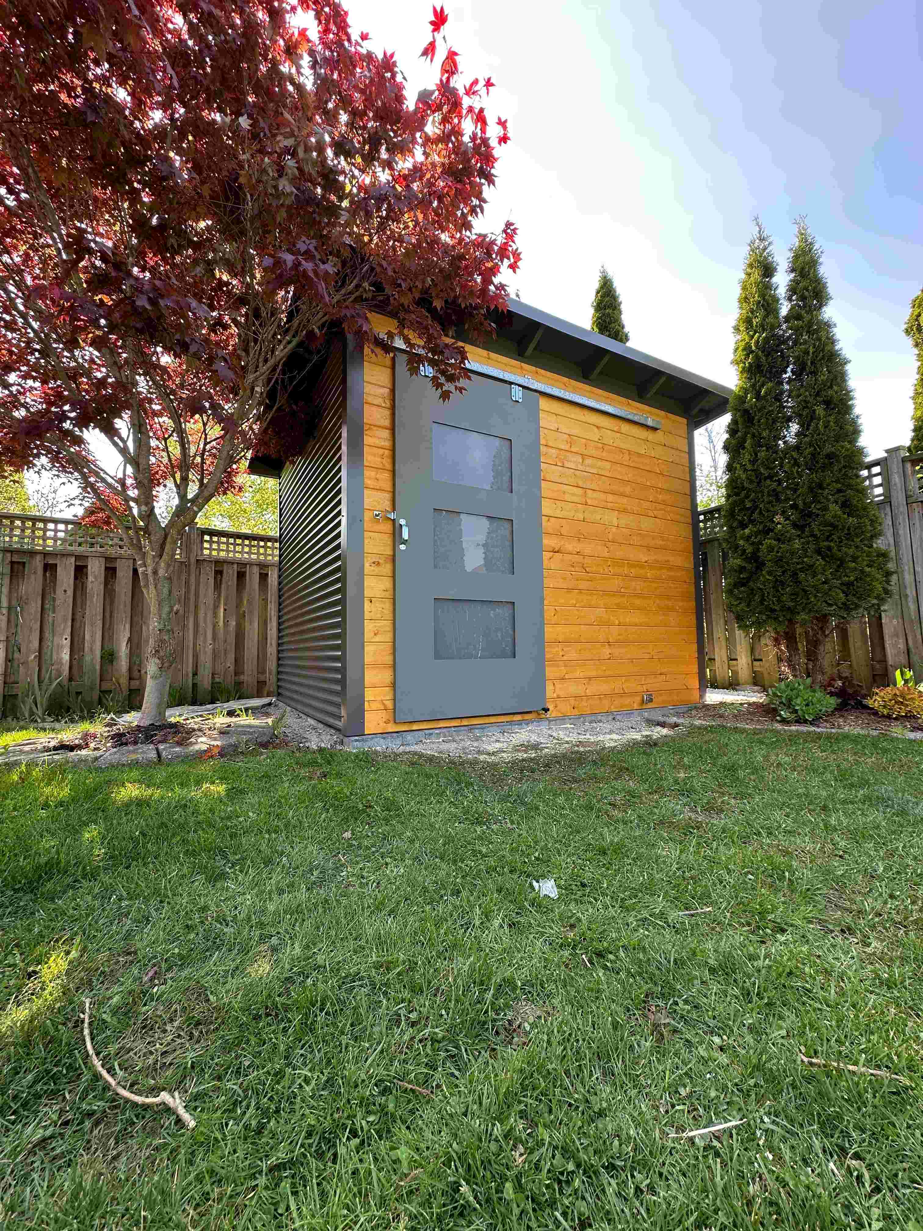 Finished 10x8 Essential Shed in London Ontario with Black Beauty sliding barn door, cedar stain pine front wall, and charcoal corrugated steel siding installed by Backyard Escape Studios.