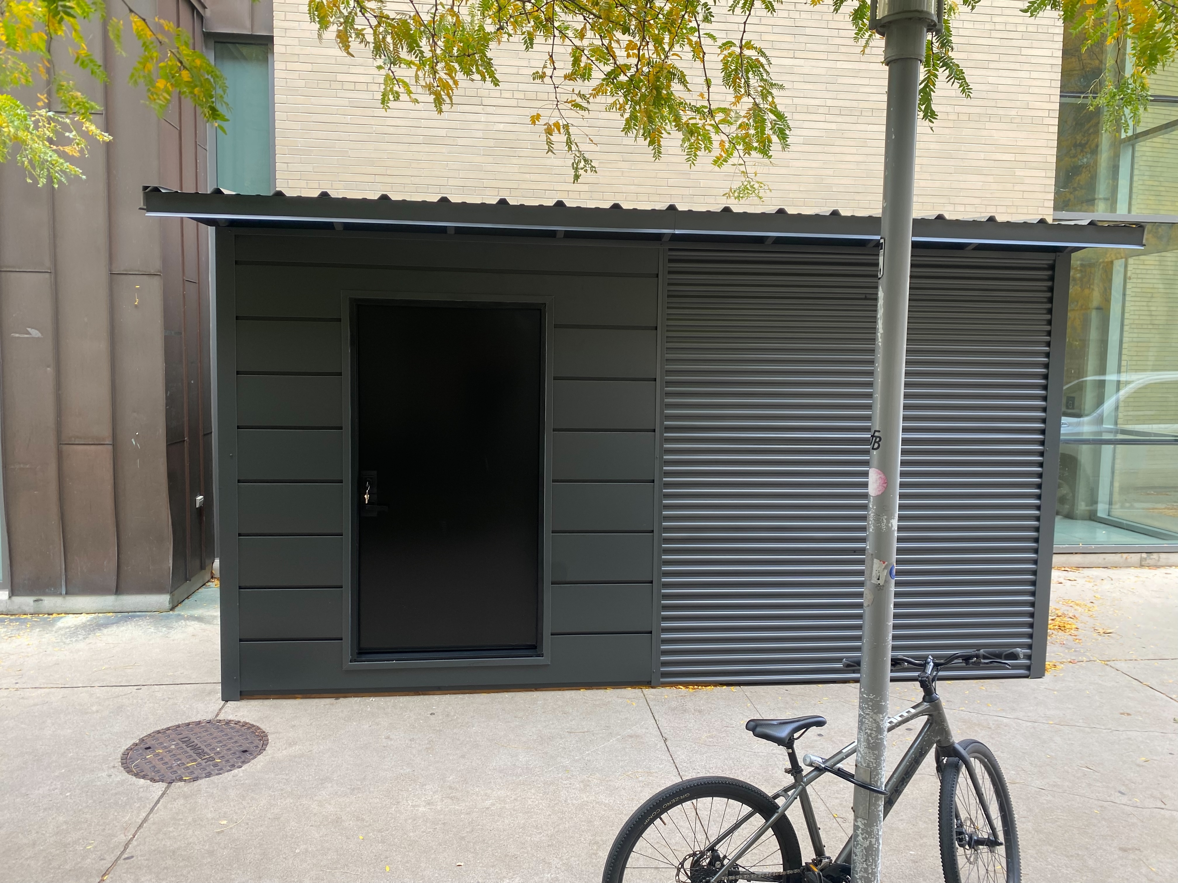 16x10 Essential Shed bike storage unit with charcoal corrugated steel siding, matching flush door, and steel roof installed at McMaster University in Hamilton Ontario by Backyard Escape Studios.