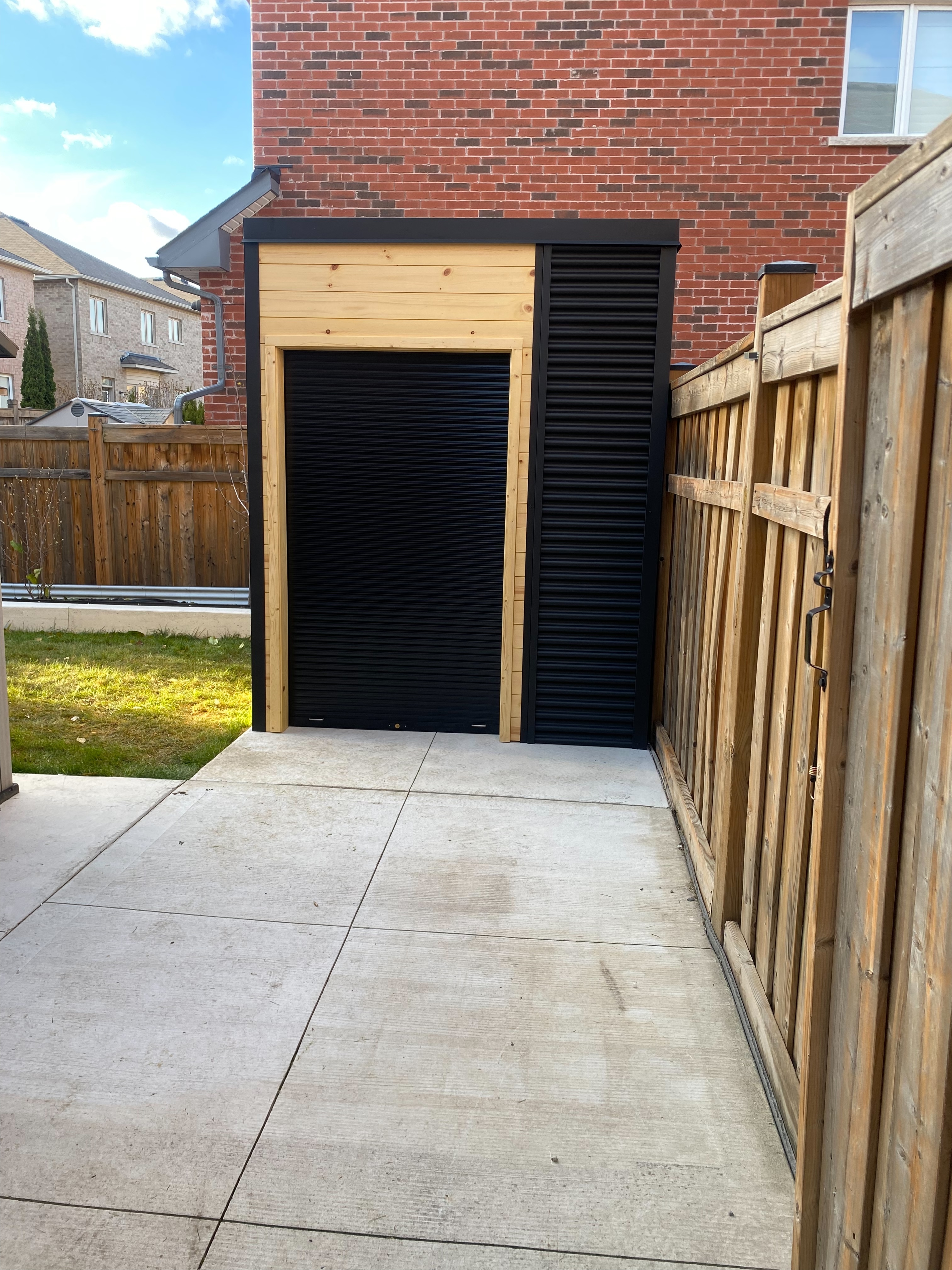 Front view of 14x7 Cube Shed in Mississauga Ontario with black aluminum roll-up shutter door, pine T&G upper panel, and Ebony corrugated steel siding, installed by Backyard Escape Studios.