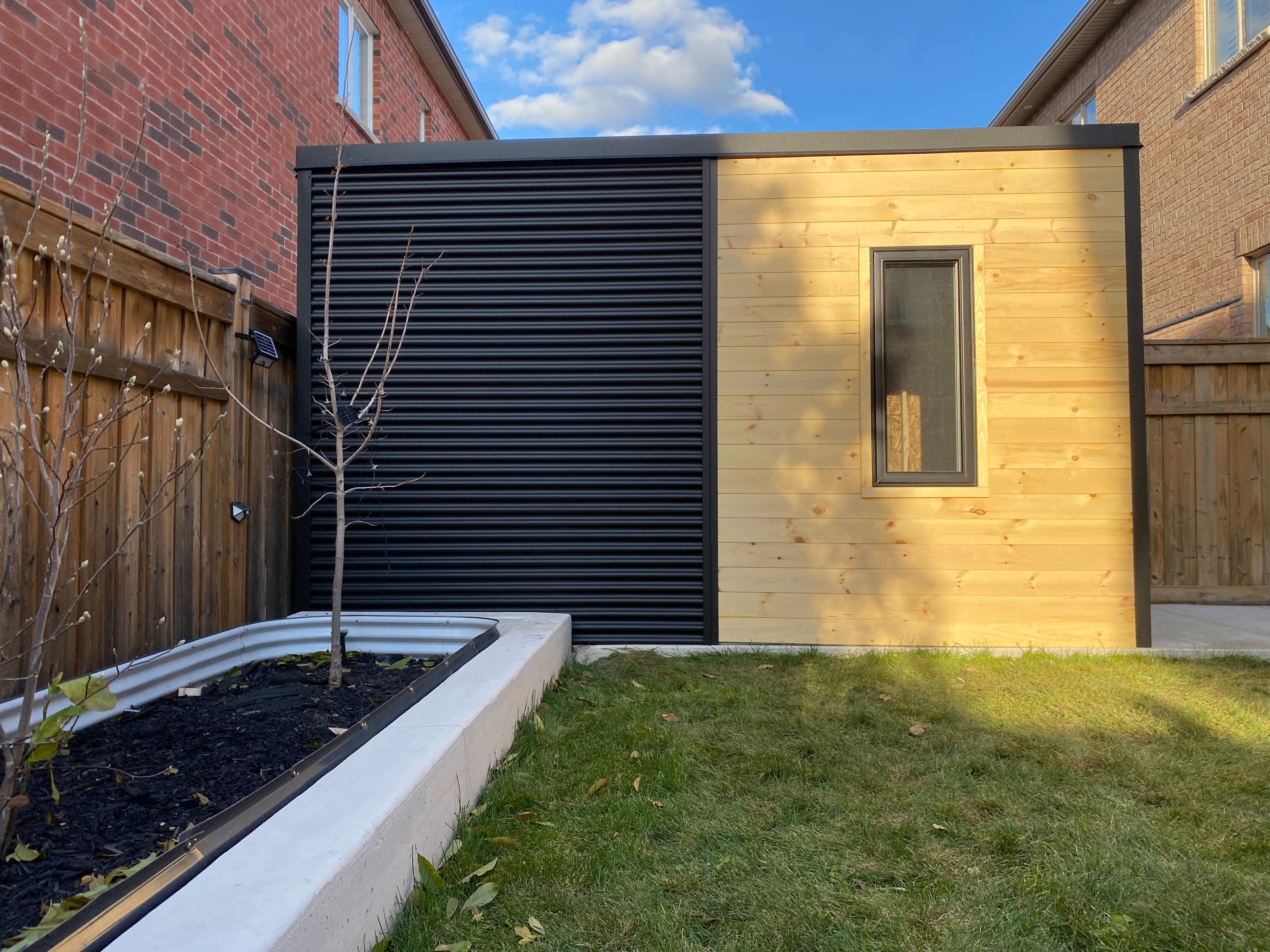 Side view of 14x7 Cube Shed in Mississauga Ontario installed in a tight urban corridor on an existing concrete pad, with Ebony corrugated steel and aluminum roll-up door, installed by Backyard Escape Studios.