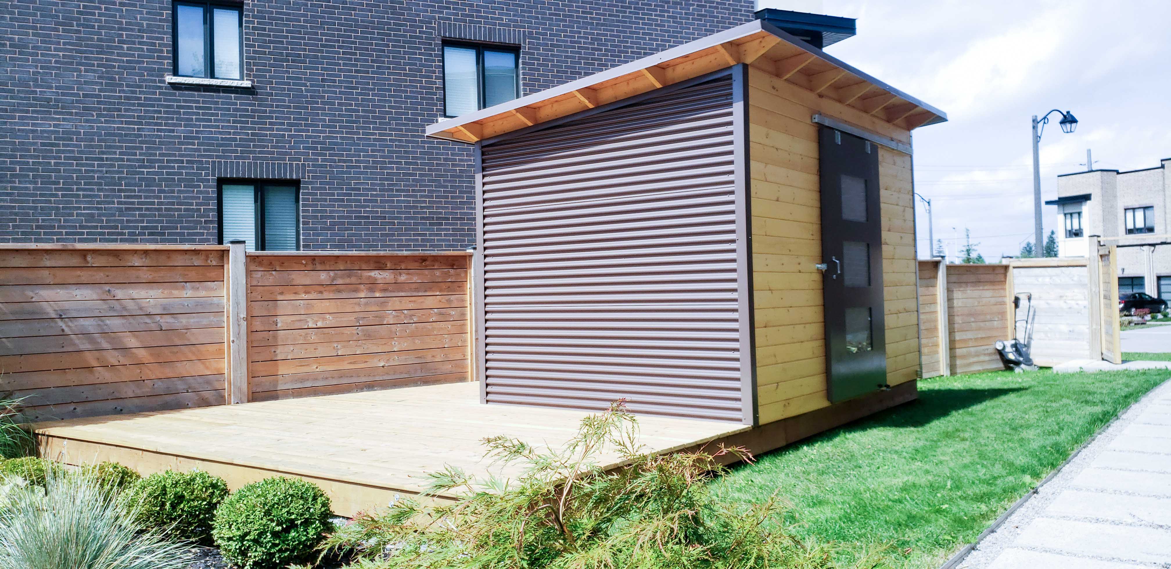 12x8 Essential garden shed with Metro Brown corrugated steel siding and teak-stained pine front wall, sliding barn door with Lexan glass panels, installed in Richmond Hill Ontario by Backyard Escape Studios.