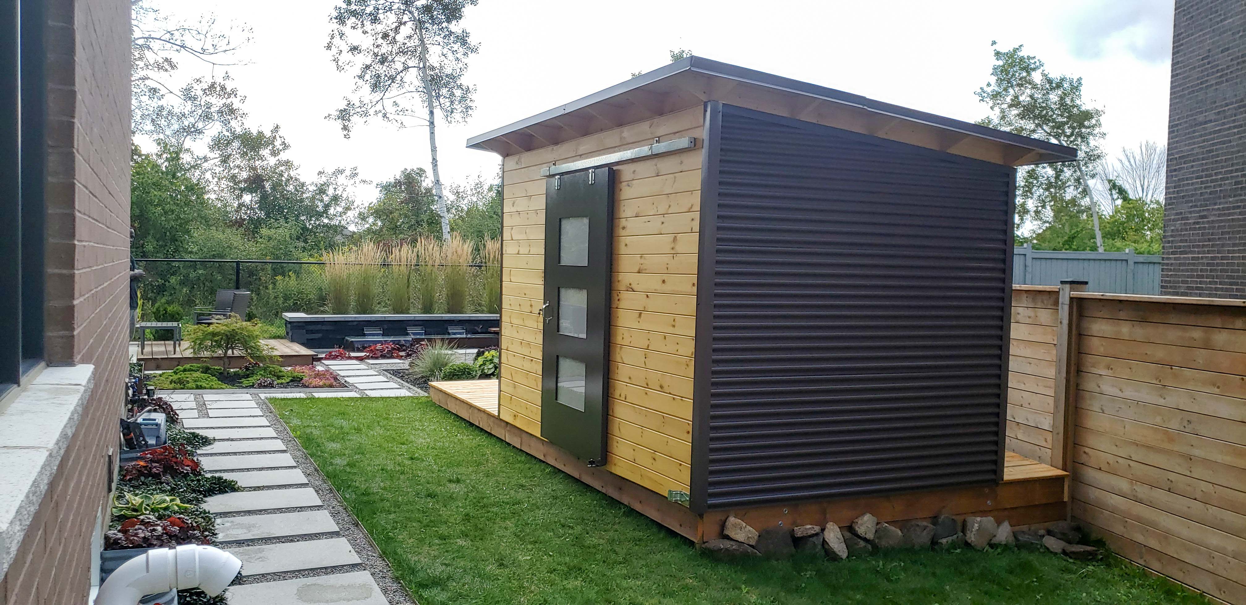 12x8 Essential garden shed with Metro Brown corrugated steel siding and teak-stained horizontal pine front wall, 48-inch sliding barn door with Lexan glass panels, installed in Richmond Hill Ontario by Backyard Escape Studios.