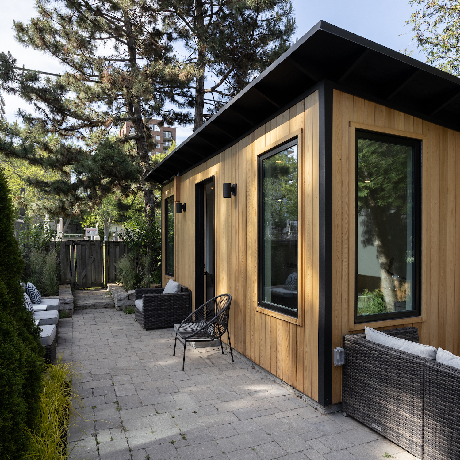 22x12 backyard cedar studio with clear cedar siding, black corrugated steel trim, and black porch lights installed in a downtown Toronto Ontario backyard by Backyard Escape Studios