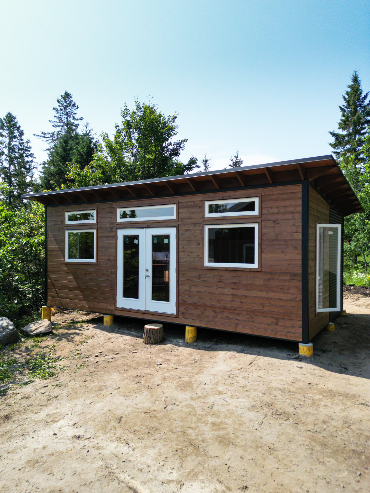 25x14 luxury cottage bunkie with Muskoka Brown pine shiplap siding, white French doors, and exposed rafter tails in a wooded North Bay Ontario setting by Backyard Escape Studios