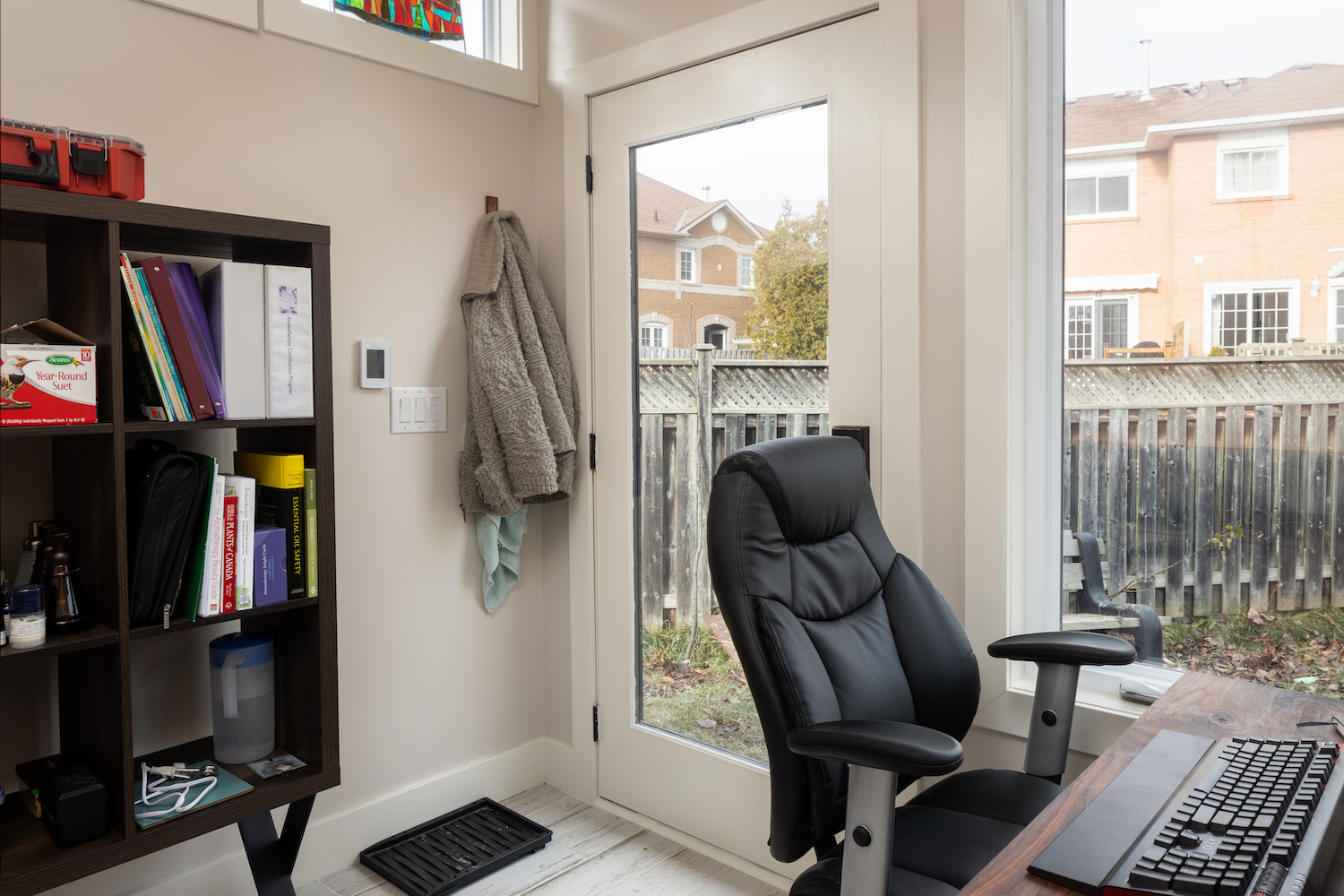Interior of a 9x9 backyard home office with white finished walls, windowed door, office desk setup, bookshelf, and track lighting in Mississauga Ontario