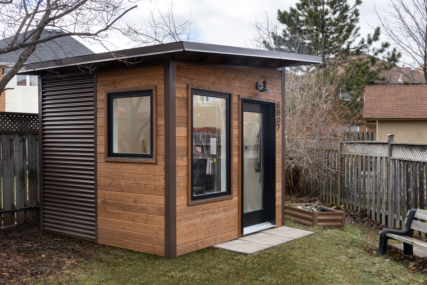 Front view of a 9x9 backyard home office with pine shiplap, large black-framed window, full-lite door, and barn light in Mississauga Ontario