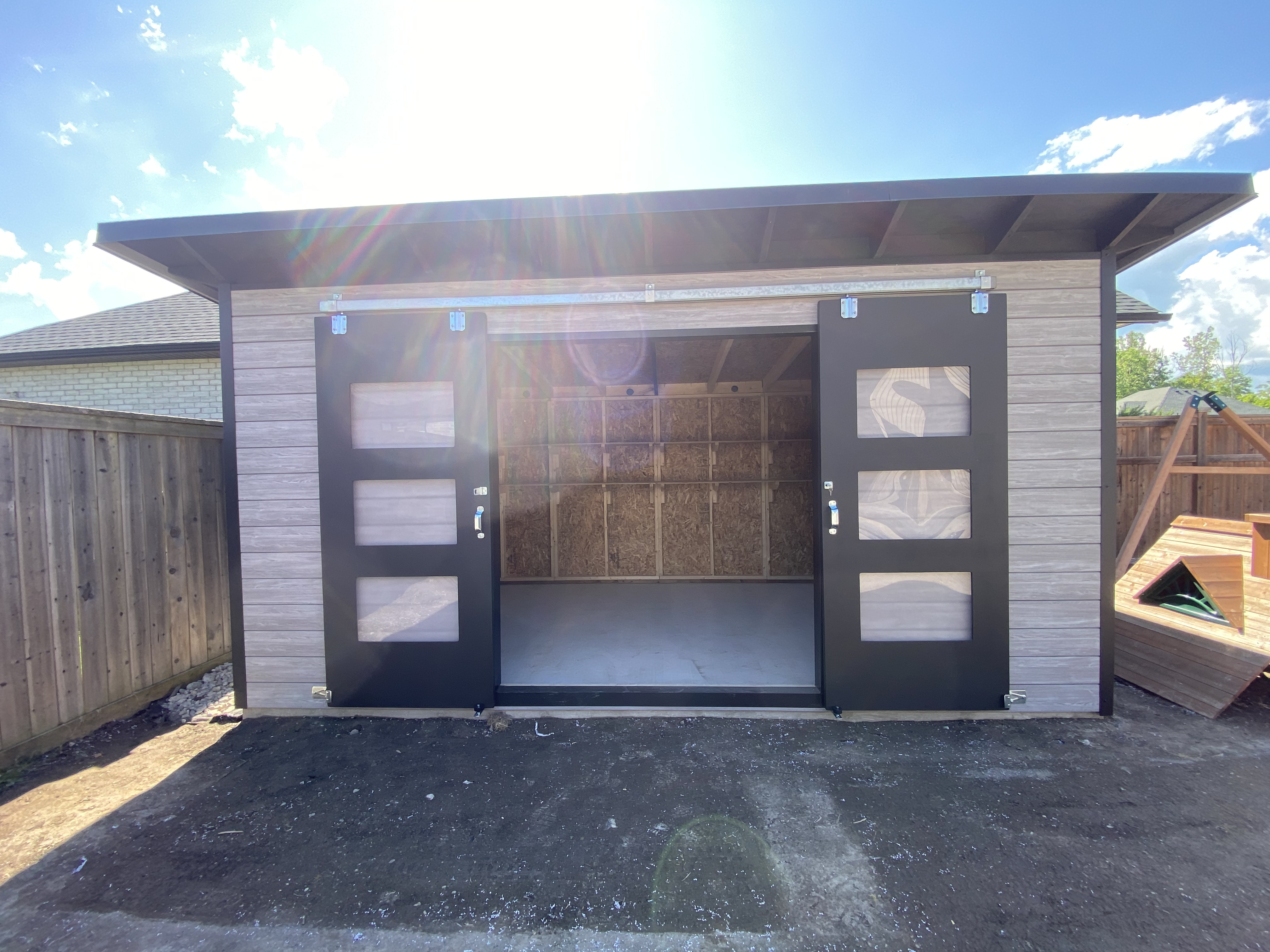 Front elevation of a 16x10 Essential Storage Shed in Sarnia, Ontario with Barnboard Grey Chamclad shiplap and Black Beauty sliding barn doors installed by Backyard Escape Studios.