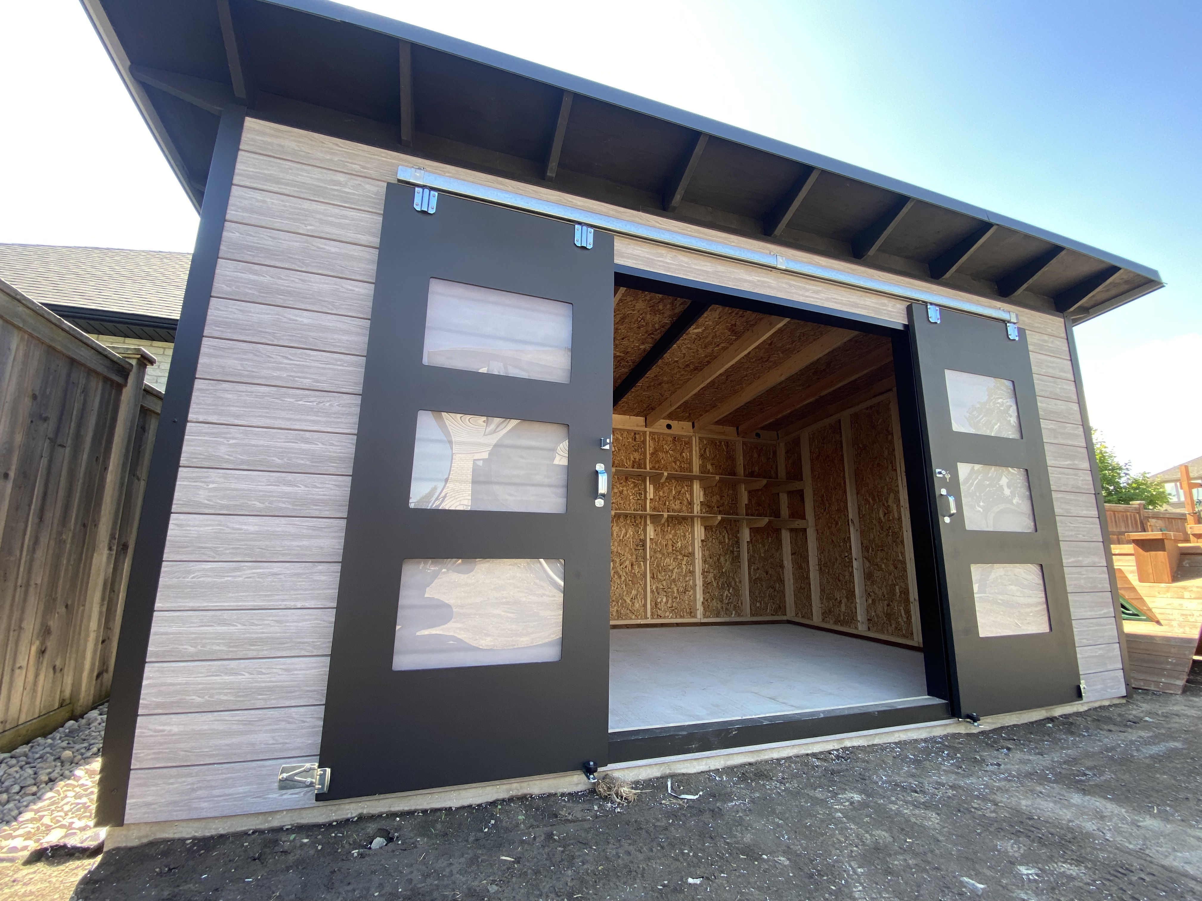 Front elevation of a 16x10 Essential Storage Shed in Sarnia, Ontario with Barnboard Grey Chamclad shiplap and Black Beauty sliding barn doors installed by Backyard Escape Studios.