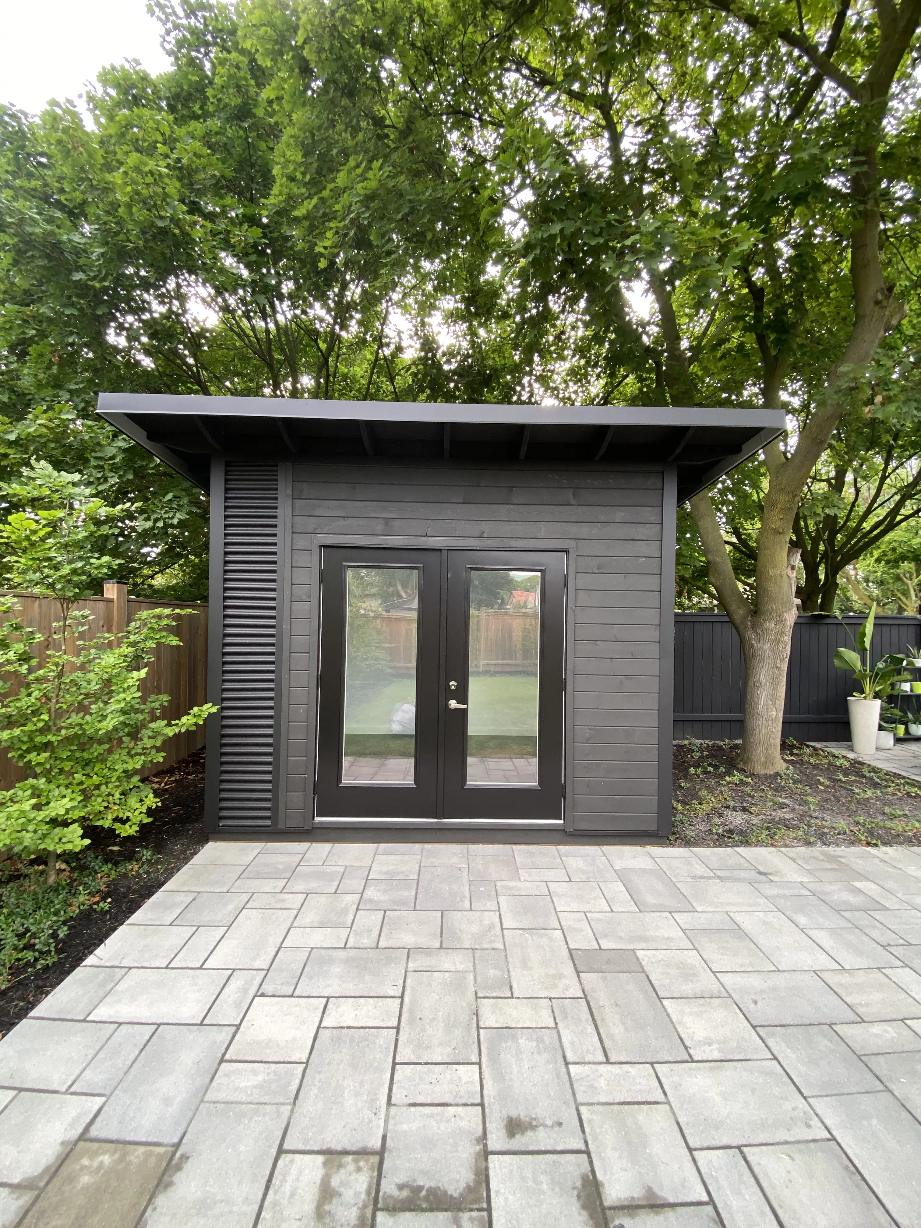 11x9 Backyard Office Studio with jet black corrugated steel siding, Black Beauty stained pine T+G front wall, and black French doors with clear glass in St. Catharines, Ontario, installed by Backyard Escape Studios.