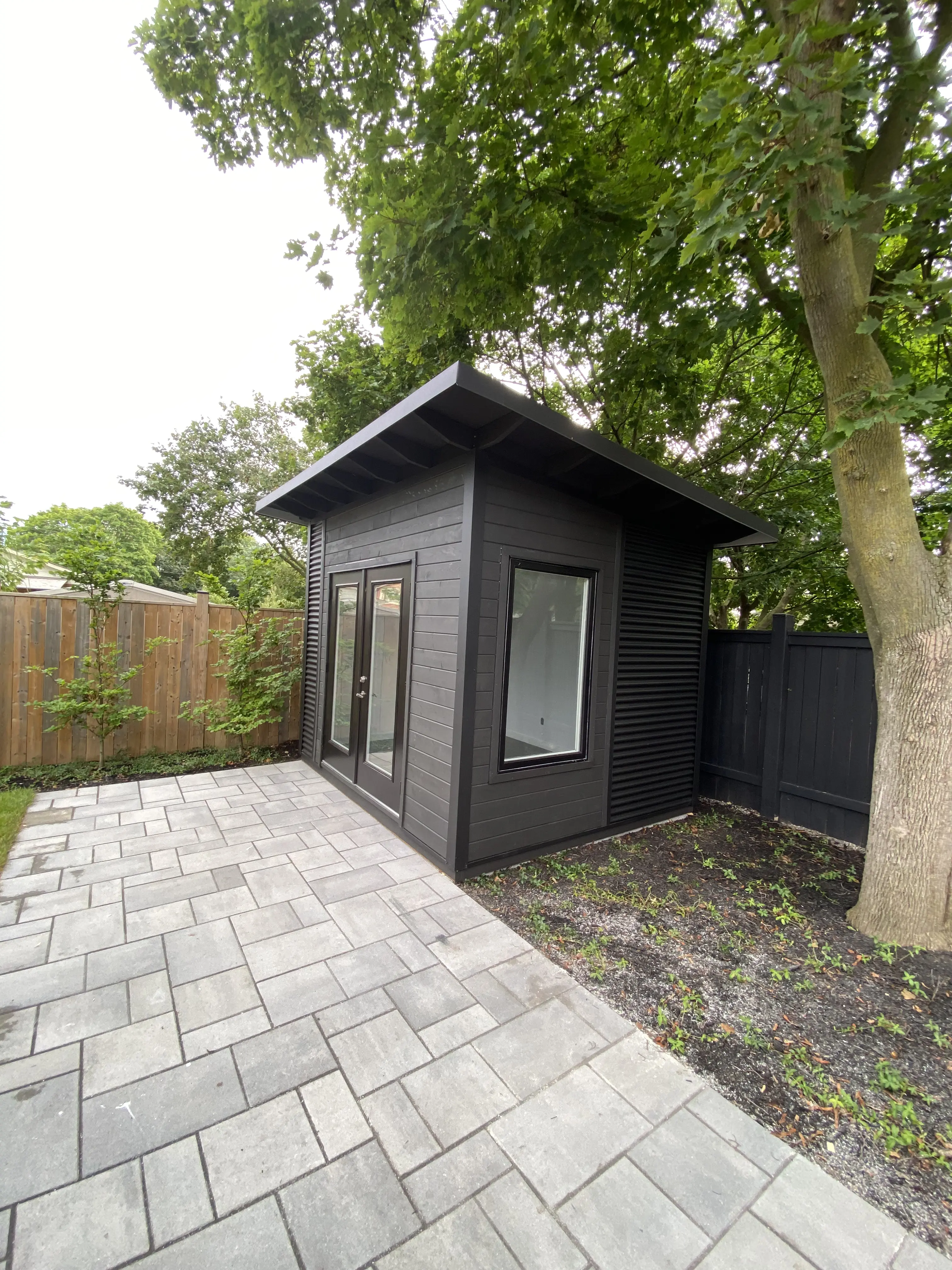 Alt: 11x9 Backyard Office Studio with Black Beauty stained pine T+G front wall, jet black corrugated steel side wall, and 36x60 black casement window in St. Catharines, Ontario.