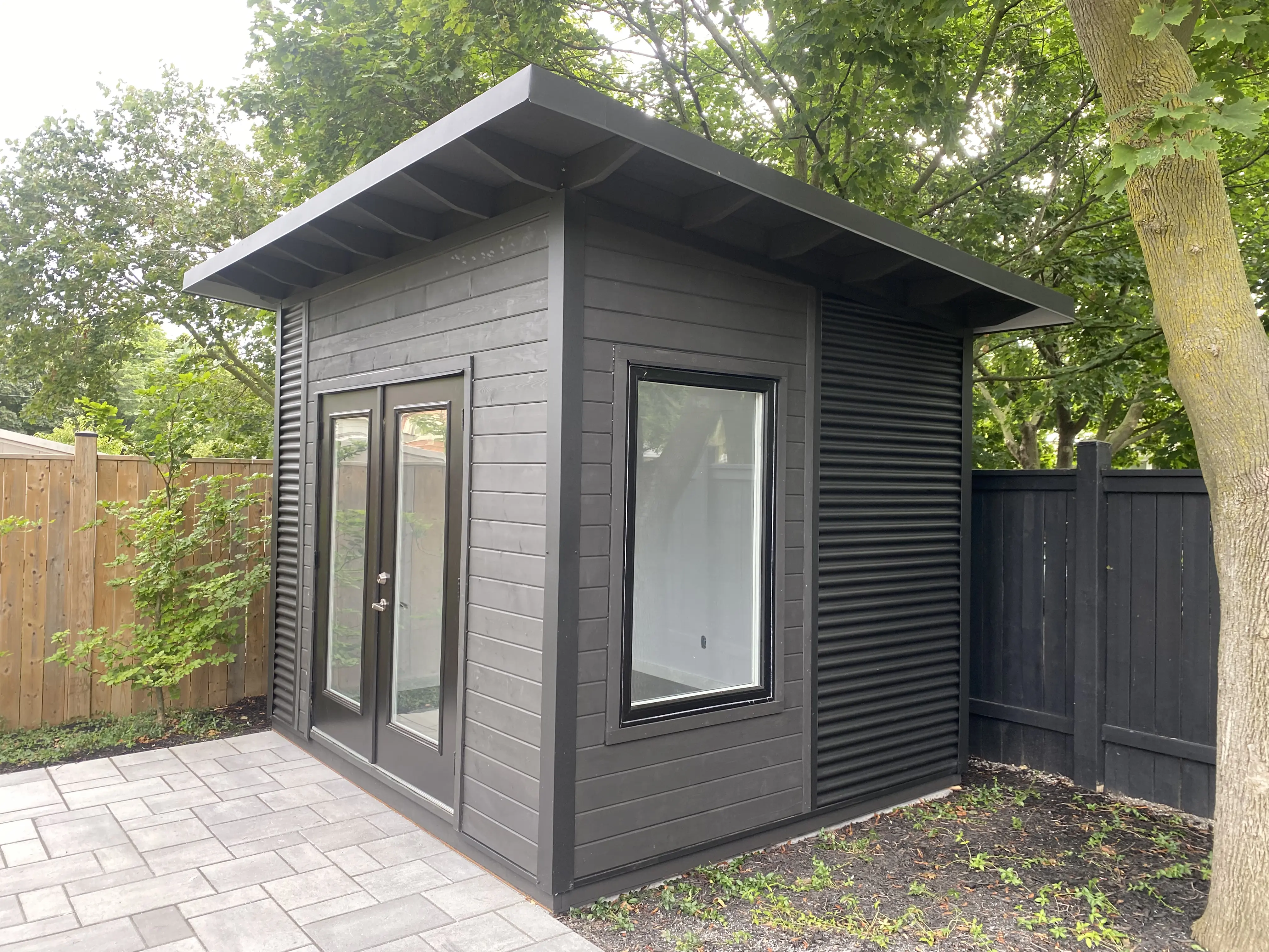 Alt: Backyard Office Studio exterior in St. Catharines, Ontario with jet black corrugated steel siding, exposed black-painted rafters, and deep roof overhangs by Backyard Escape Studios.