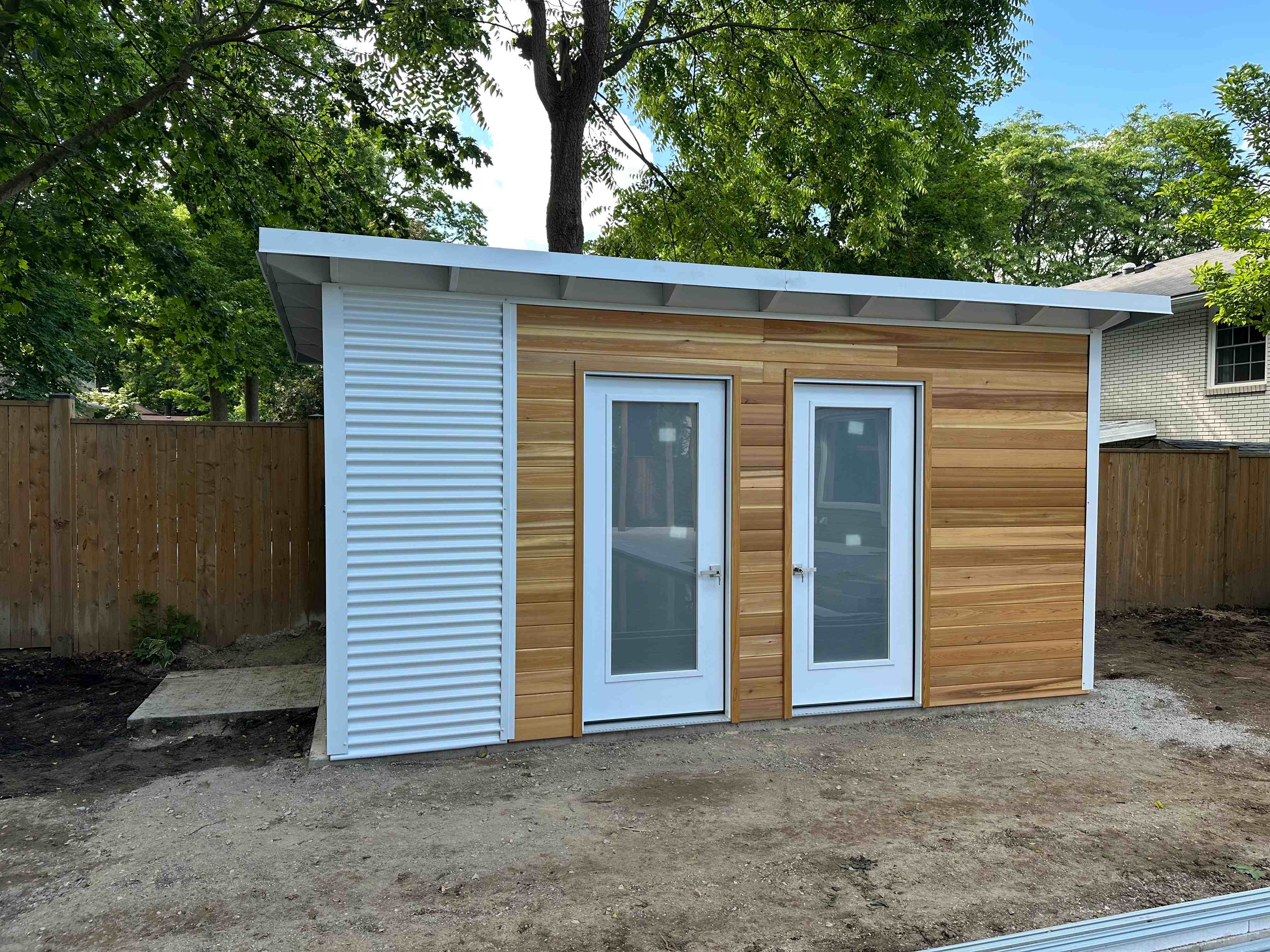 16x10 Pool Shed in London, Ontario with a western red cedar front and Cambridge White corrugated steel sides, an Essential Shed with two frosted glass doors installed by Backyard Escape Studios.