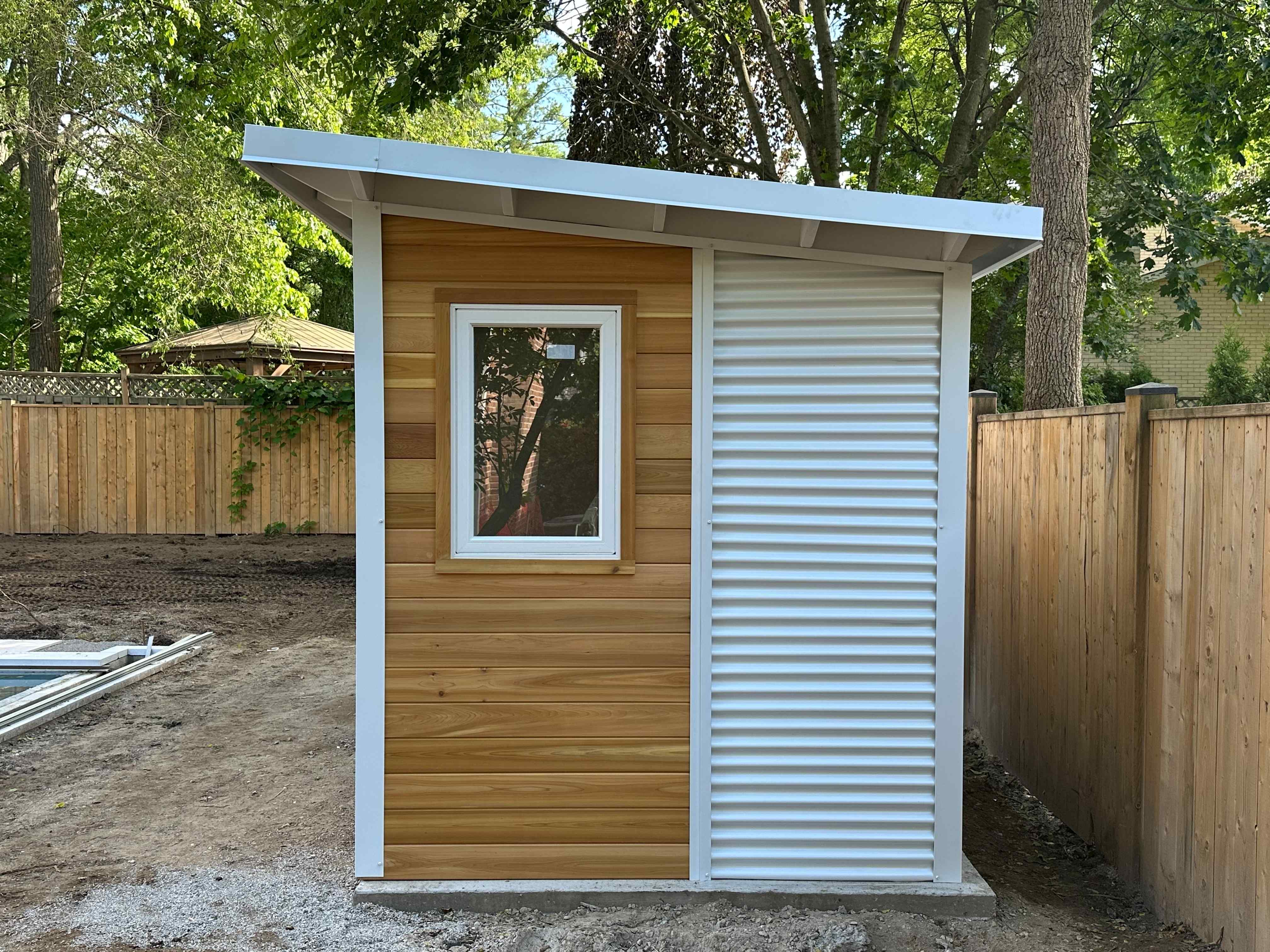 16x10 Pool Shed in London, Ontario with western red cedar front wall and two frosted glass doors installed beside an inground pool by Backyard Escape Studios.