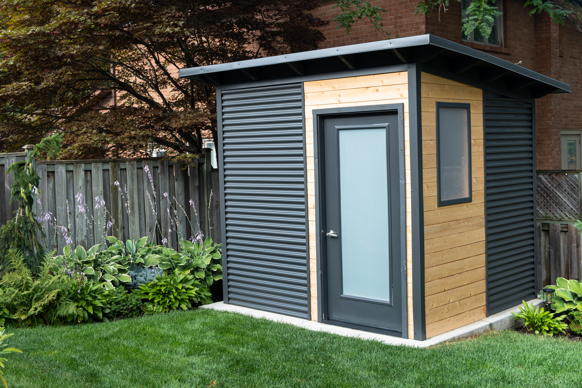 8x8 Garden Shed in Etobicoke Ontario with Iron Ore corrugated steel siding and Eastern White Cedar accent panel, an Essential Shed installed by Backyard Escape Studios.