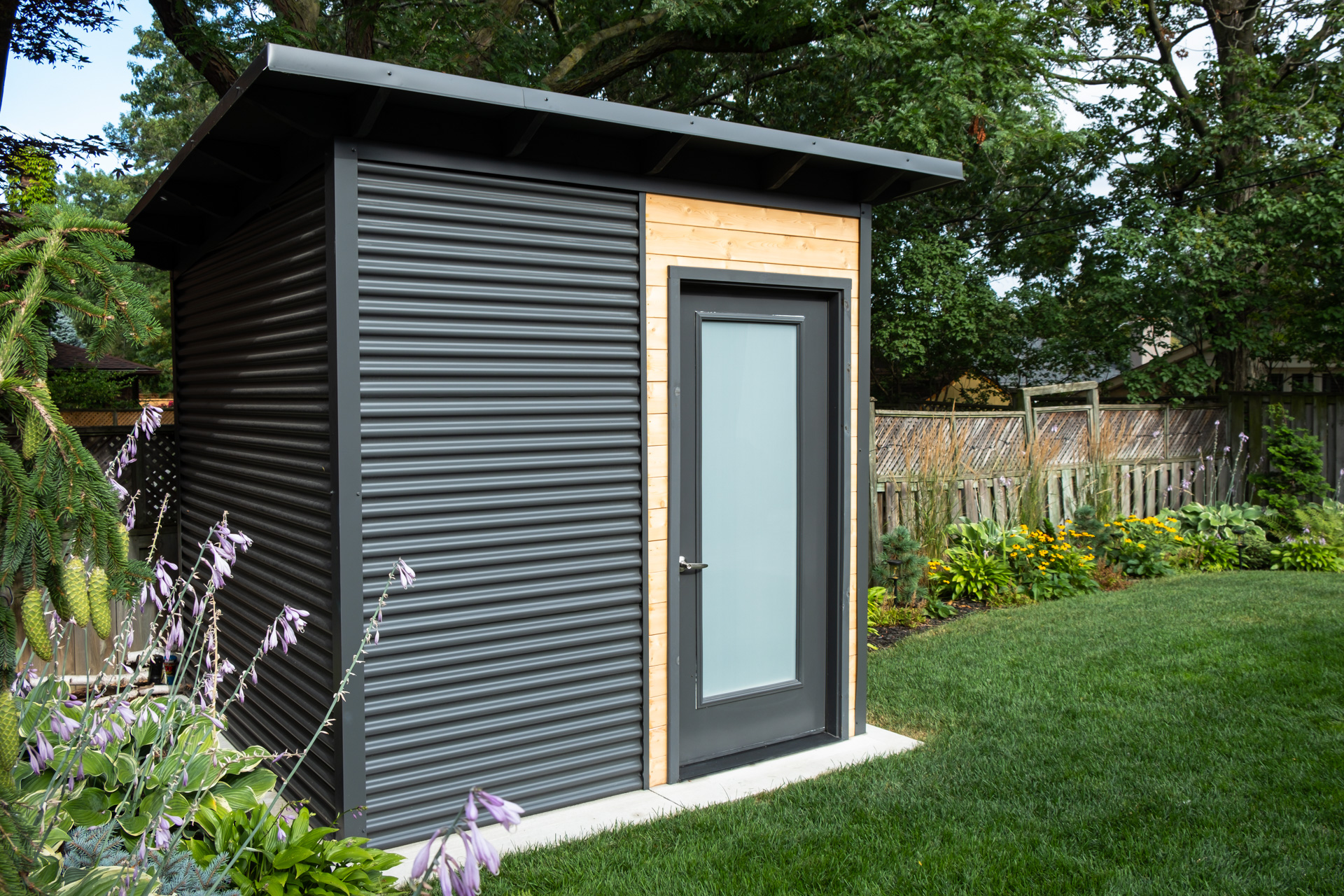 Rear corner of an 8x8 Garden Shed in Etobicoke Ontario clad in Iron Ore corrugated steel siding, an Essential Shed installed by Backyard Escape Studios.