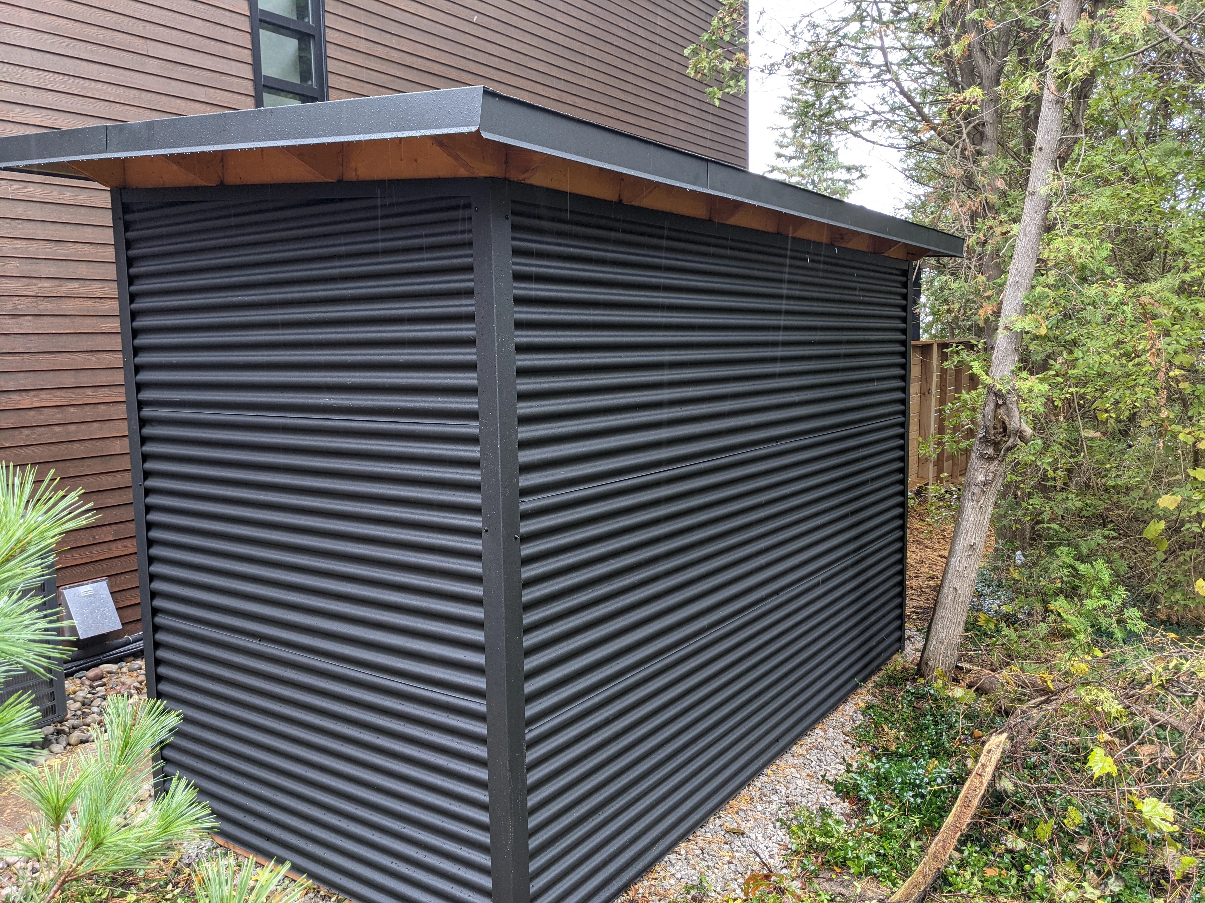 12x6 Storage Shed with Jet Black 7/8 inch corrugated steel siding installed alongside a modern dark-stained home in Grand Bend, Ontario by Backyard Escape Studios.