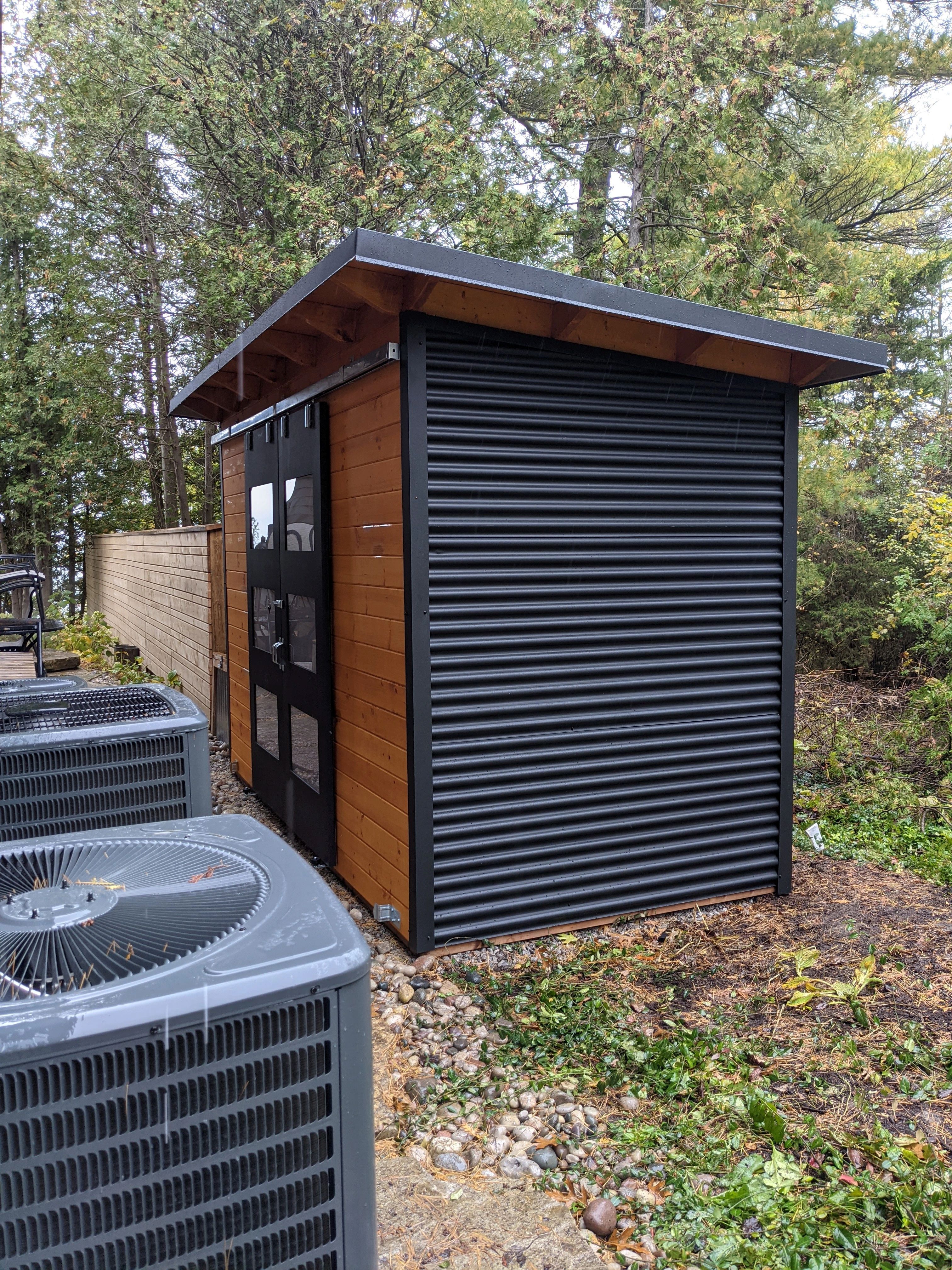 Cedar-stained pine T+G front and double sliding barn doors on a 12x6 Essential Storage Shed in Grand Bend, Ontario installed by Backyard Escape Studios.