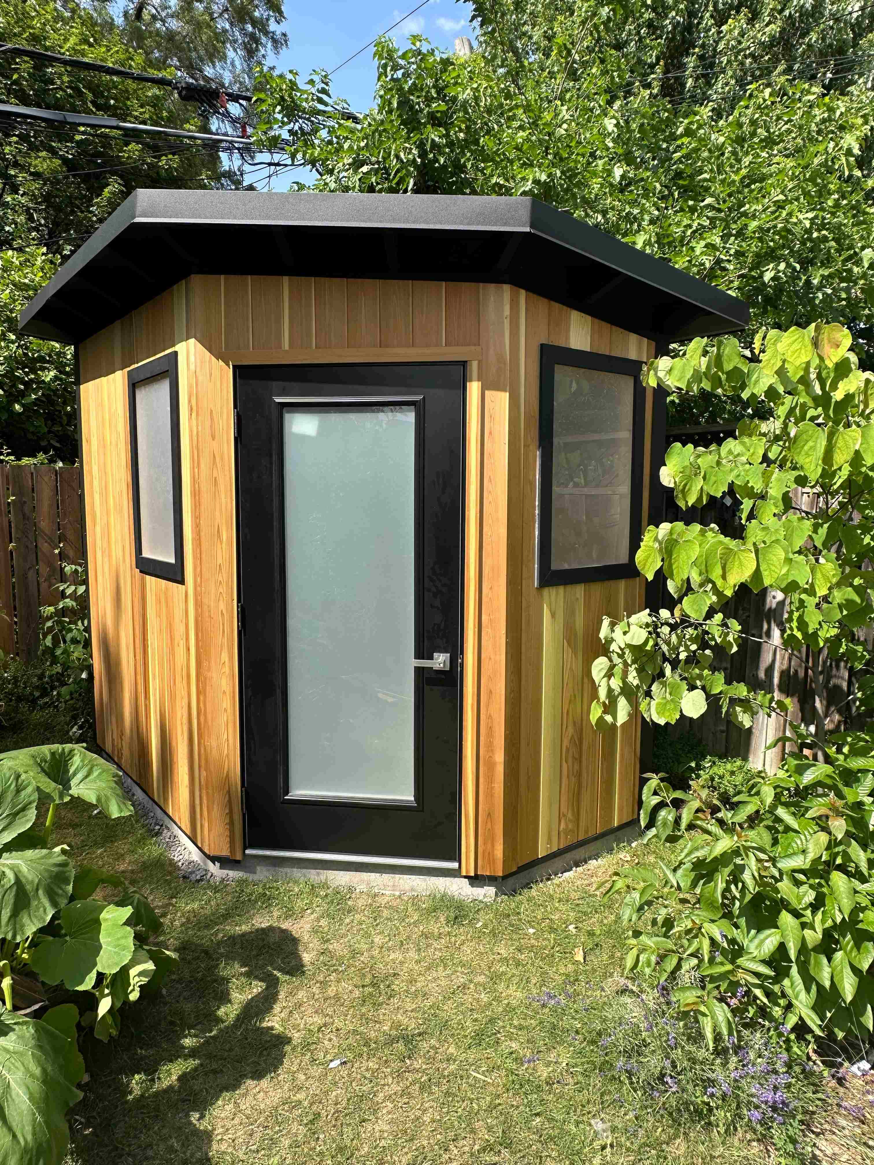 Custom 8x8 Modern Shed with a five-wall diamond footprint, vertical cedar tongue-and-groove front, and frosted glass outswing door in Etobicoke, Ontario, installed by Backyard Escape Studios.