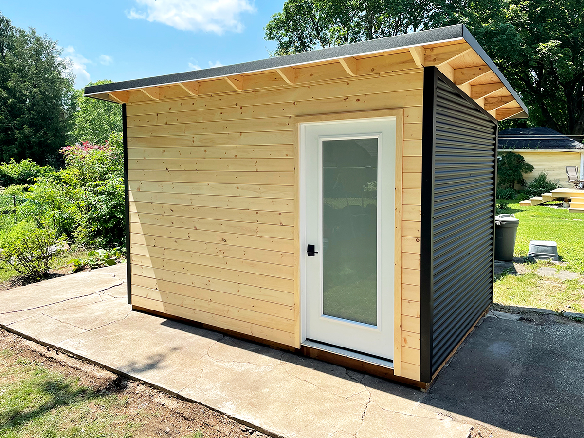 12x8 Essential Garden Shed with black corrugated steel siding and natural pine front in Stratford, Ontario, installed by Backyard Escape Studios.