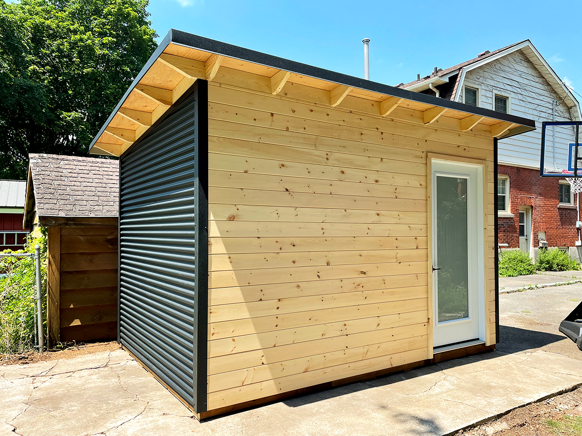 Angled view of a 12x8 Garden Shed showing black corrugated steel siding and natural pine front in Stratford, Ontario.