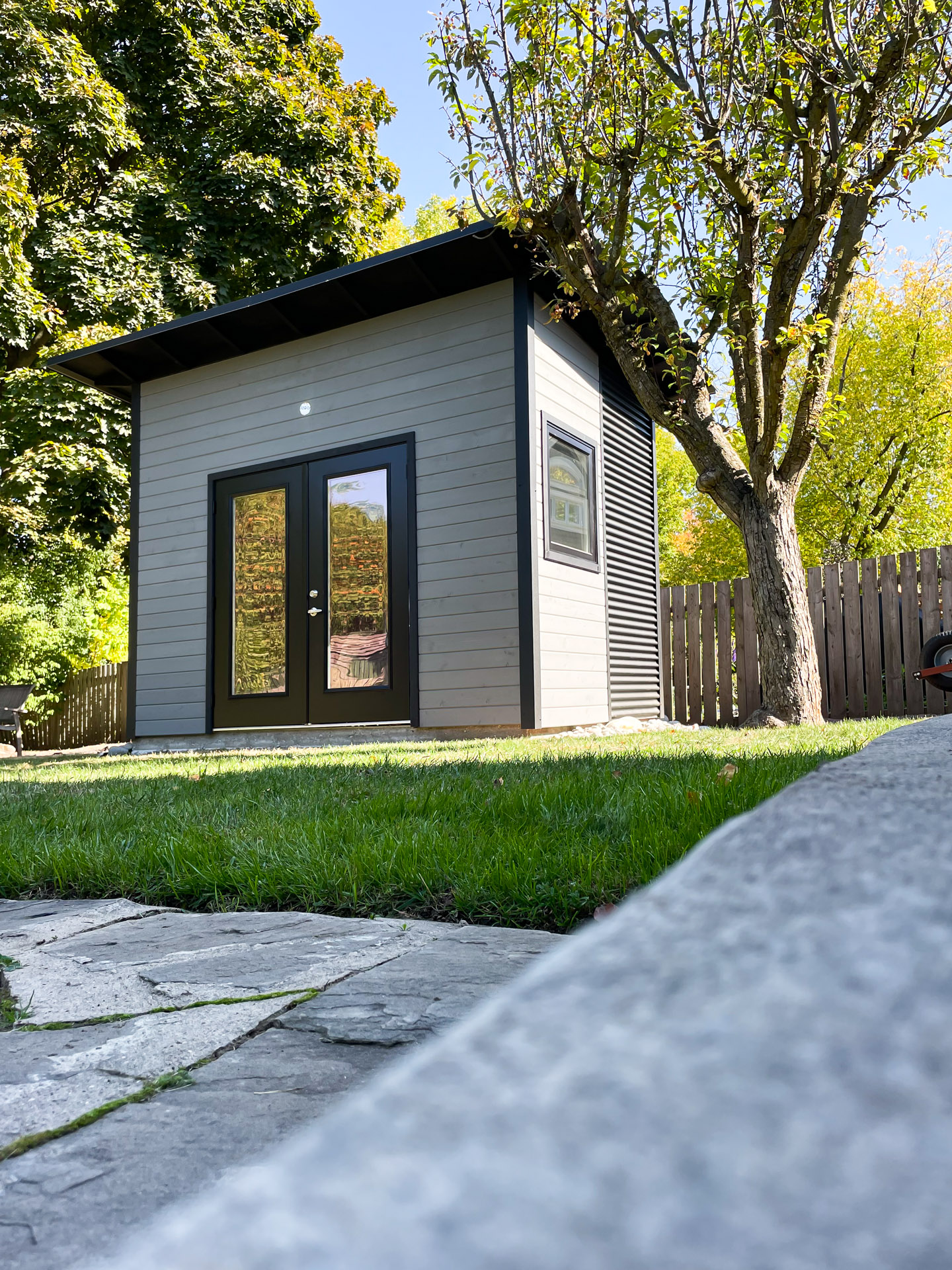 Front exterior of a 12x9 backyard studio in Oakville, Ontario, with stained pine siding, black French doors, and a skillion roof.