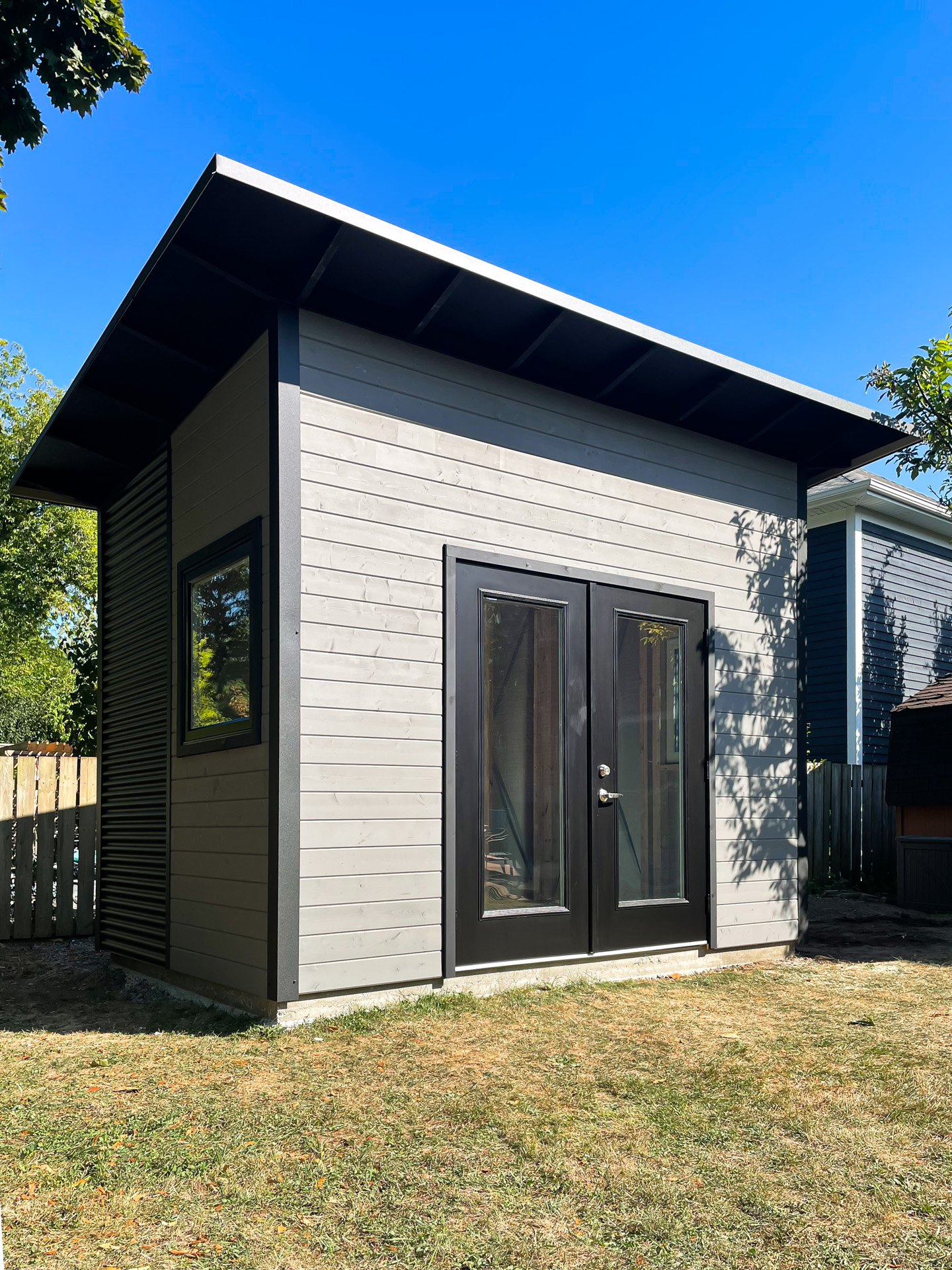 Side view of a 12x9 backyard studio in Oakville, Ontario, with Jet Black corrugated steel siding and a black-trimmed casement window.