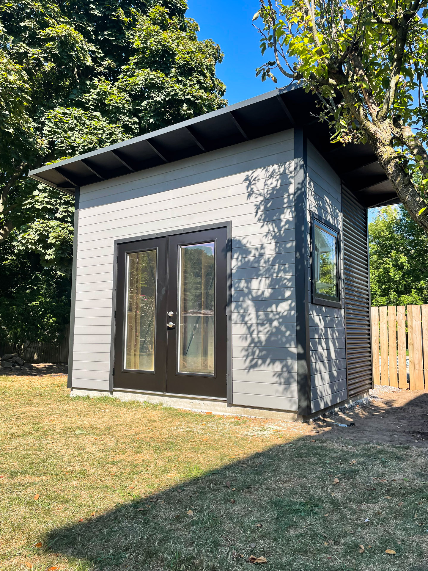 12x9 backyard studio in Oakville, Ontario, showing Jet Black corrugated steel siding, Kendall Charcoal stained pine, and black French doors.