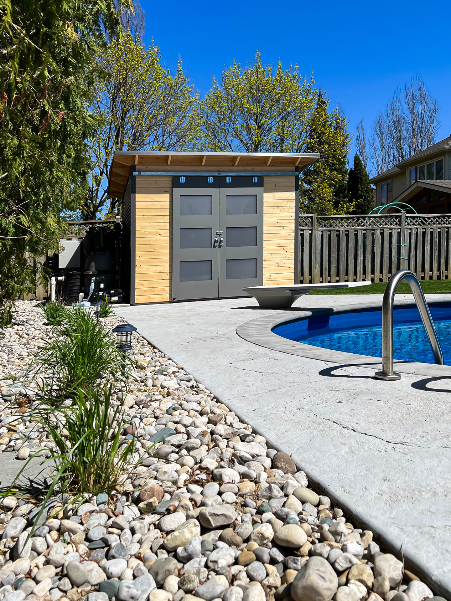 10x8 Pool Shed with charcoal steel siding and clear coat pine, Essential Shed installed poolside in London, Ontario, installed by Backyard Escape Studios.