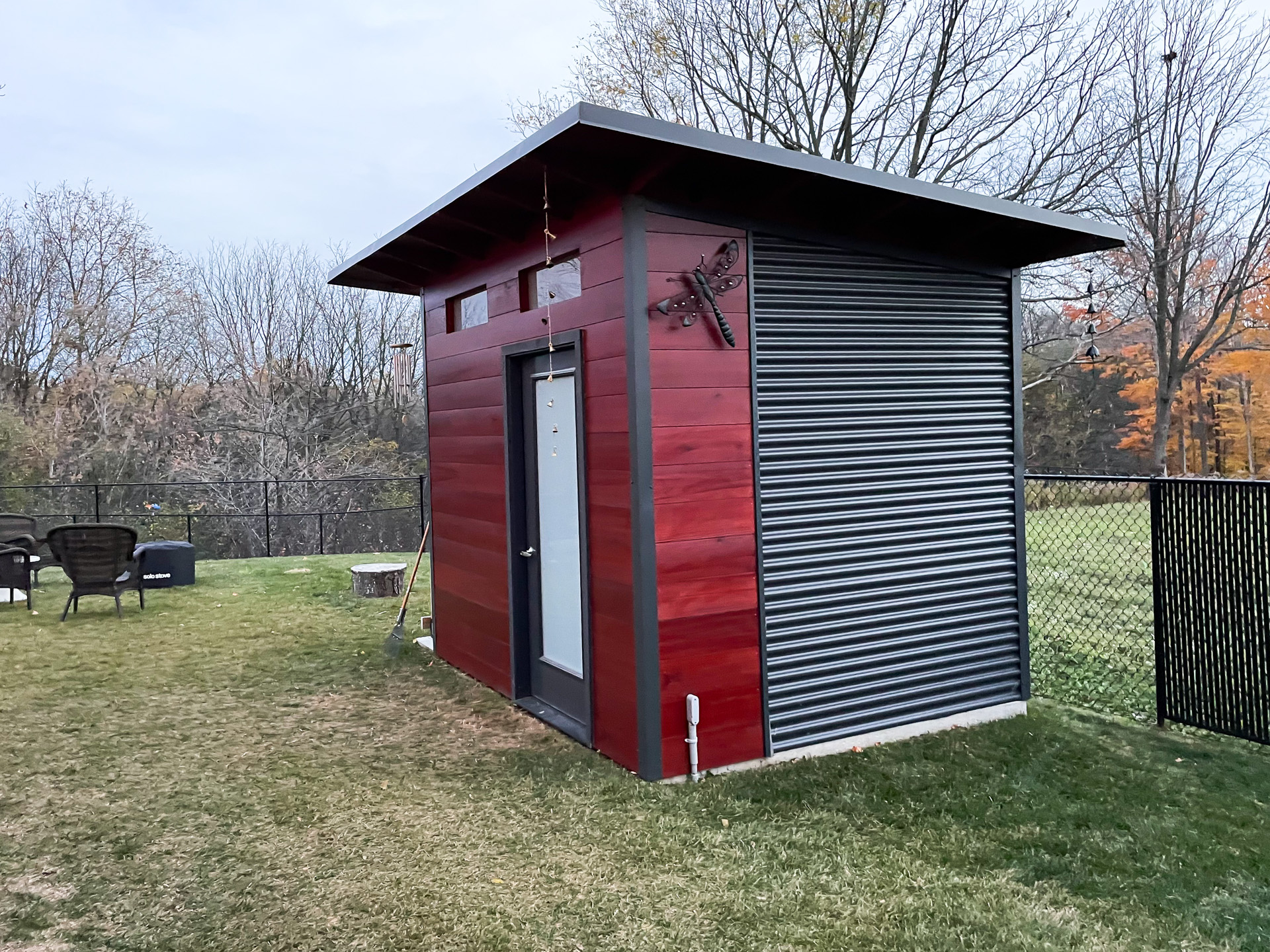 Side angle of a 10x8 modern shed in Belmont, Ontario showing Iron Ore corrugated steel siding against mahogany-stained pine