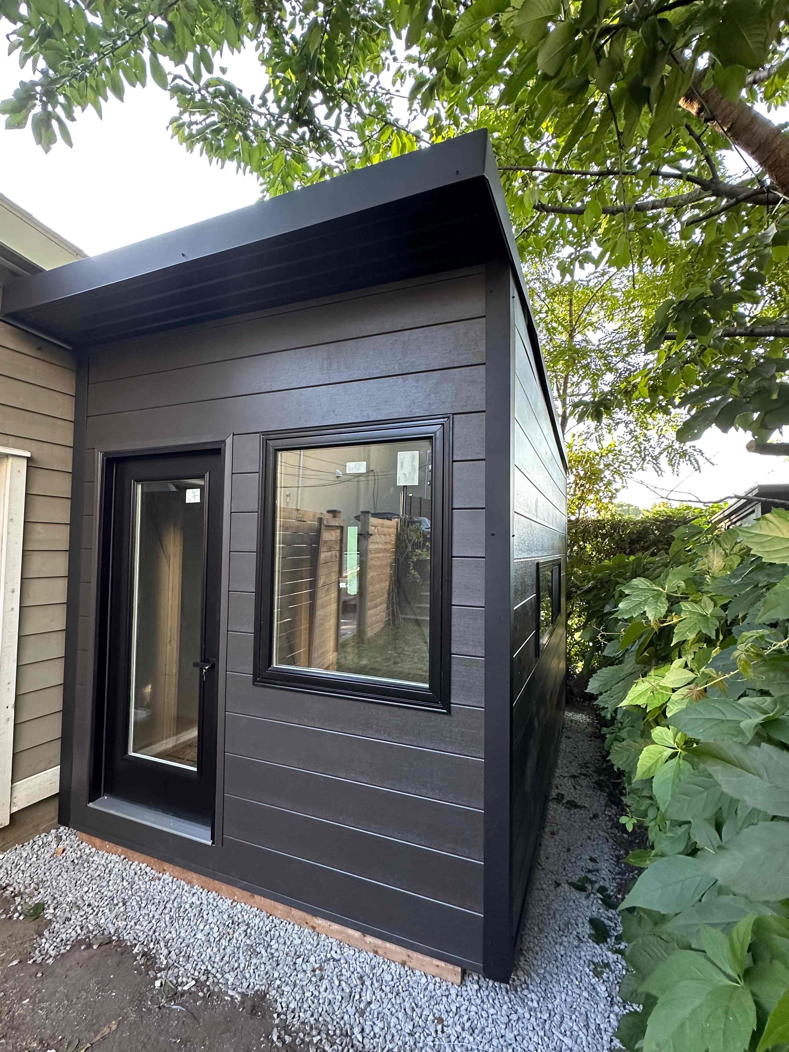 Side and corner view of a Jet Black corrugated steel backyard office studio in Scarborough, Ontario, showing the black slider window and roofline.