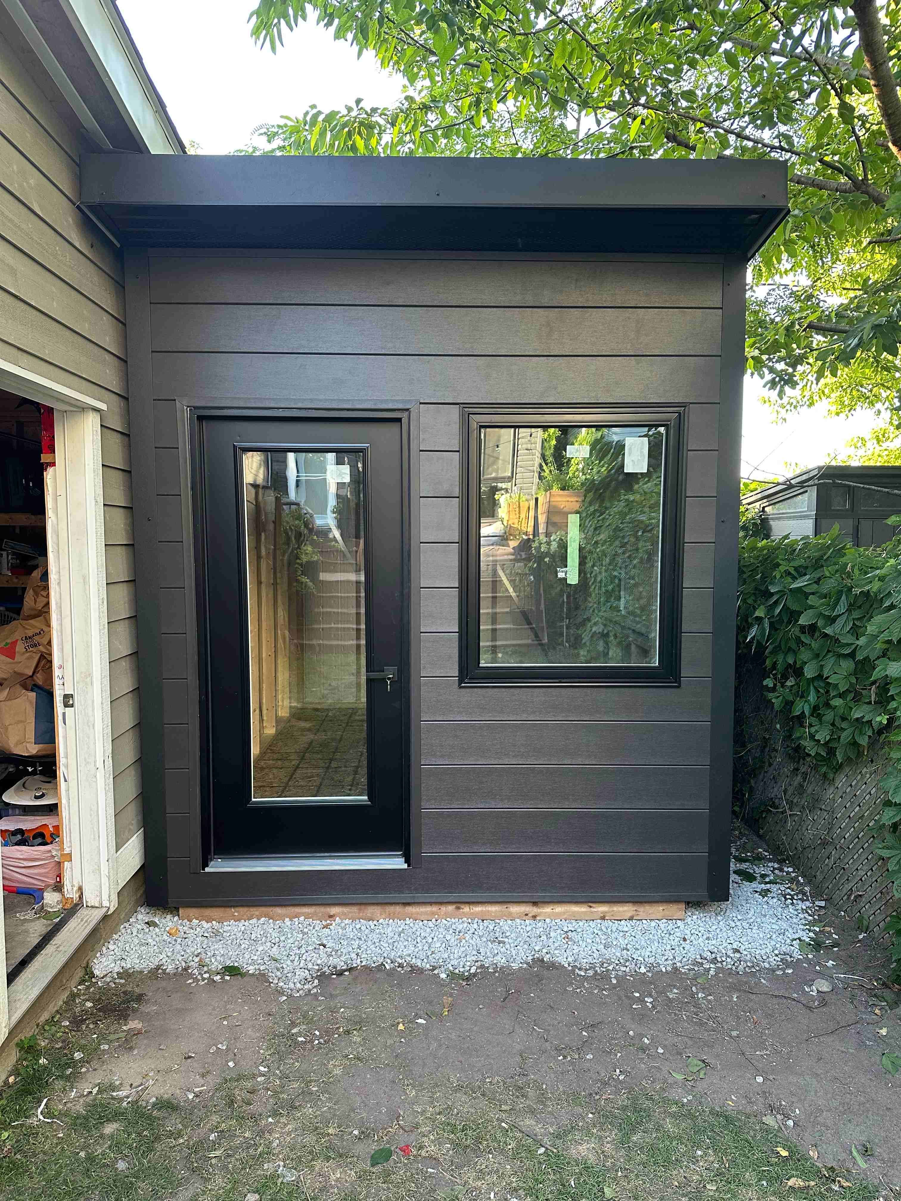 Backyard office studio installed tight against an existing garage wall in Scarborough, Ontario, showing the fitted clearance and black entry door.