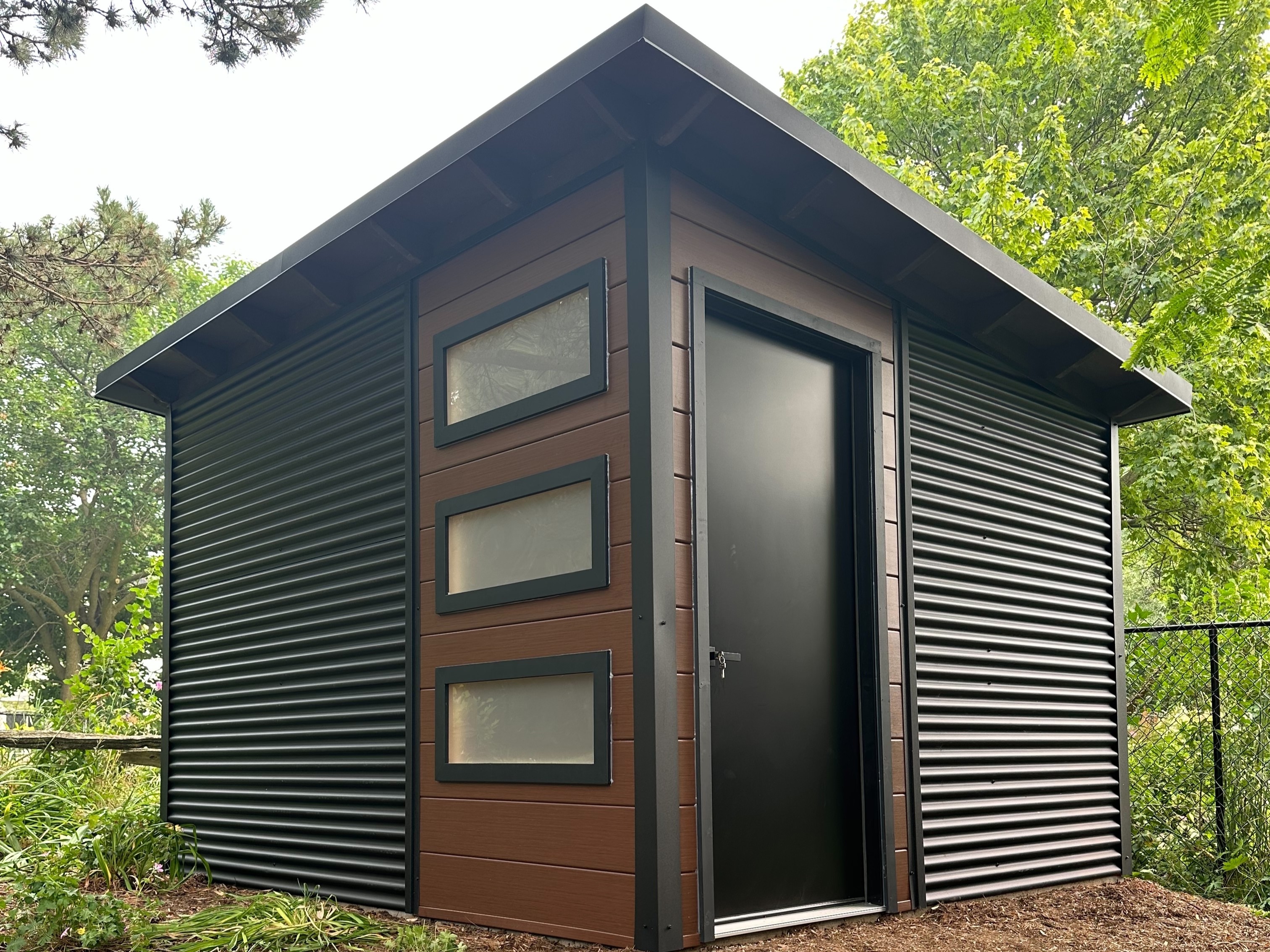 12x10 modern Essential Shed with Jet Black corrugated steel siding and Teak vinyl front wall in Waterloo, Ontario, installed by Backyard Escape Studios.