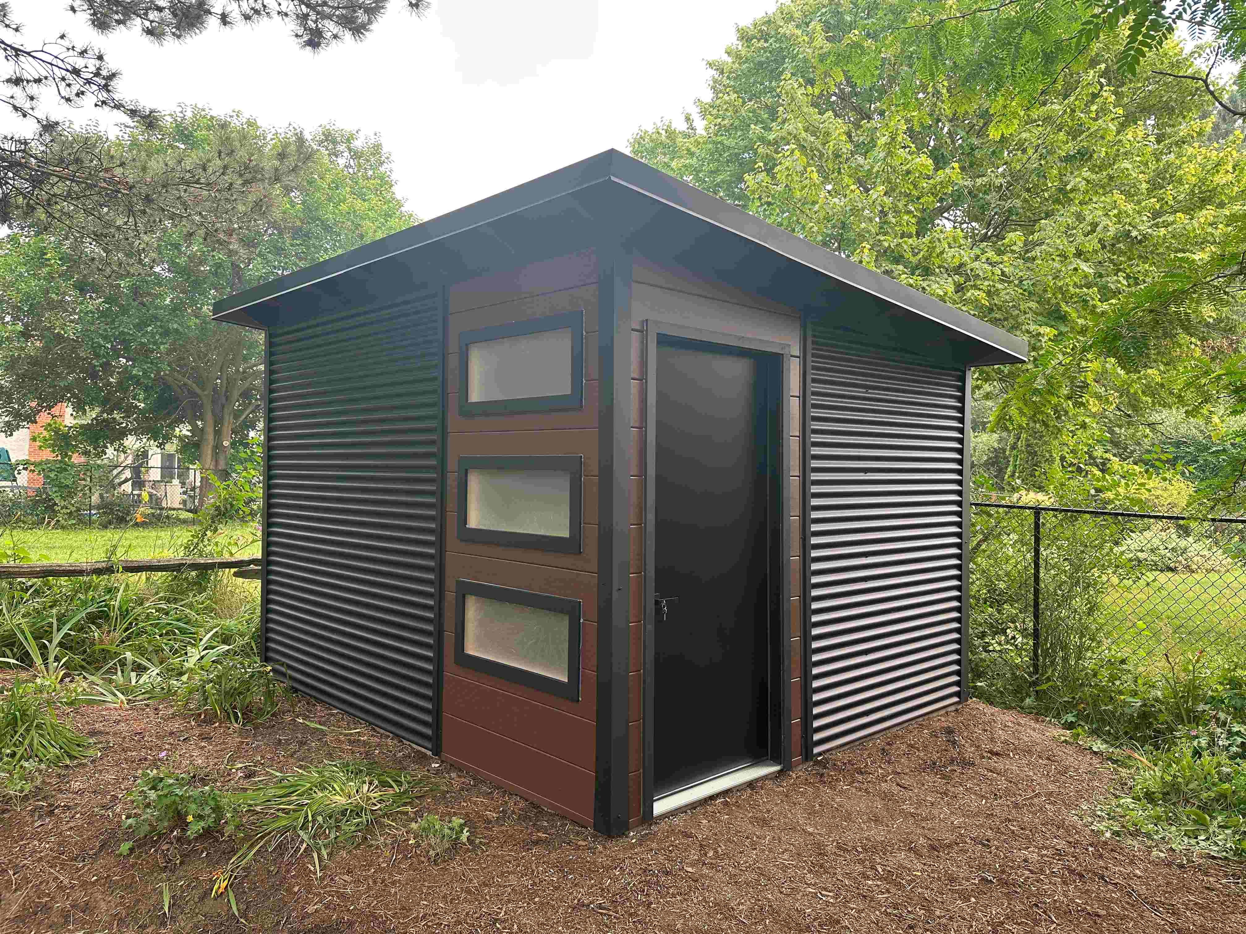 Front view of a 12x10 Essential Shed in Waterloo, Ontario, with three stacked frosted Lexan windows and a solid black steel door.