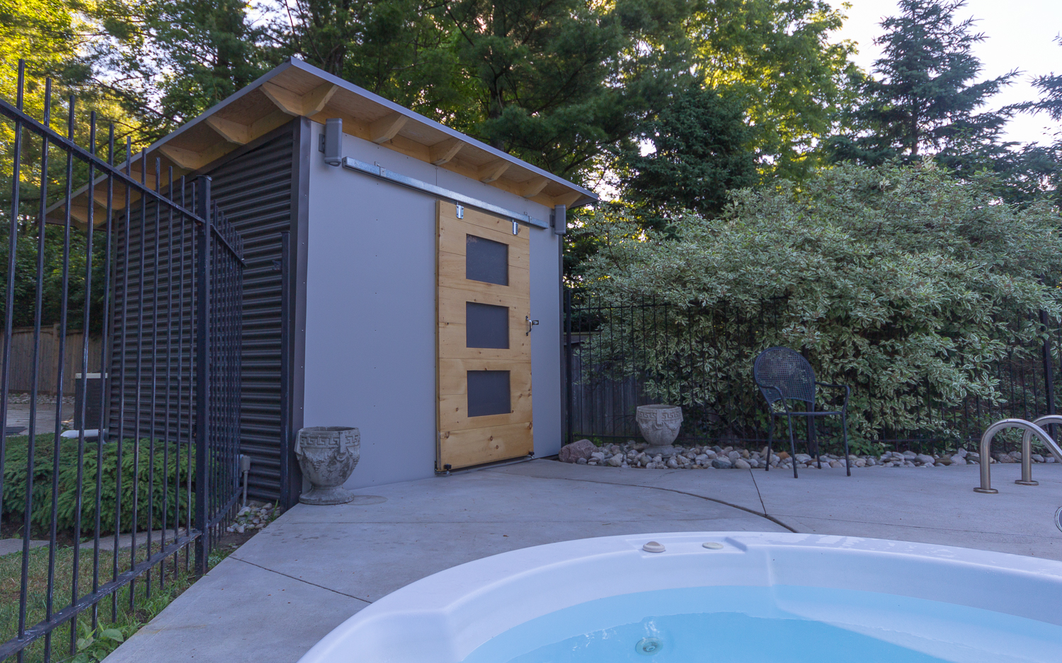 12x8 Essential Pool Shed with charcoal corrugated metal siding along a pool fence in London, Ontario