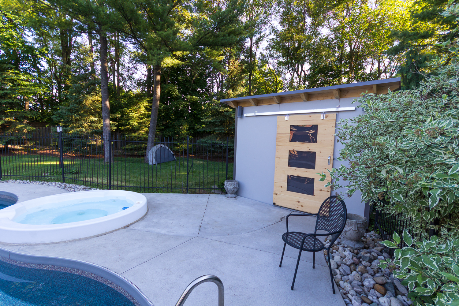 12x8 Essential Pool Shed with natural pine barn door and charcoal siding beside a pool in London, Ontario