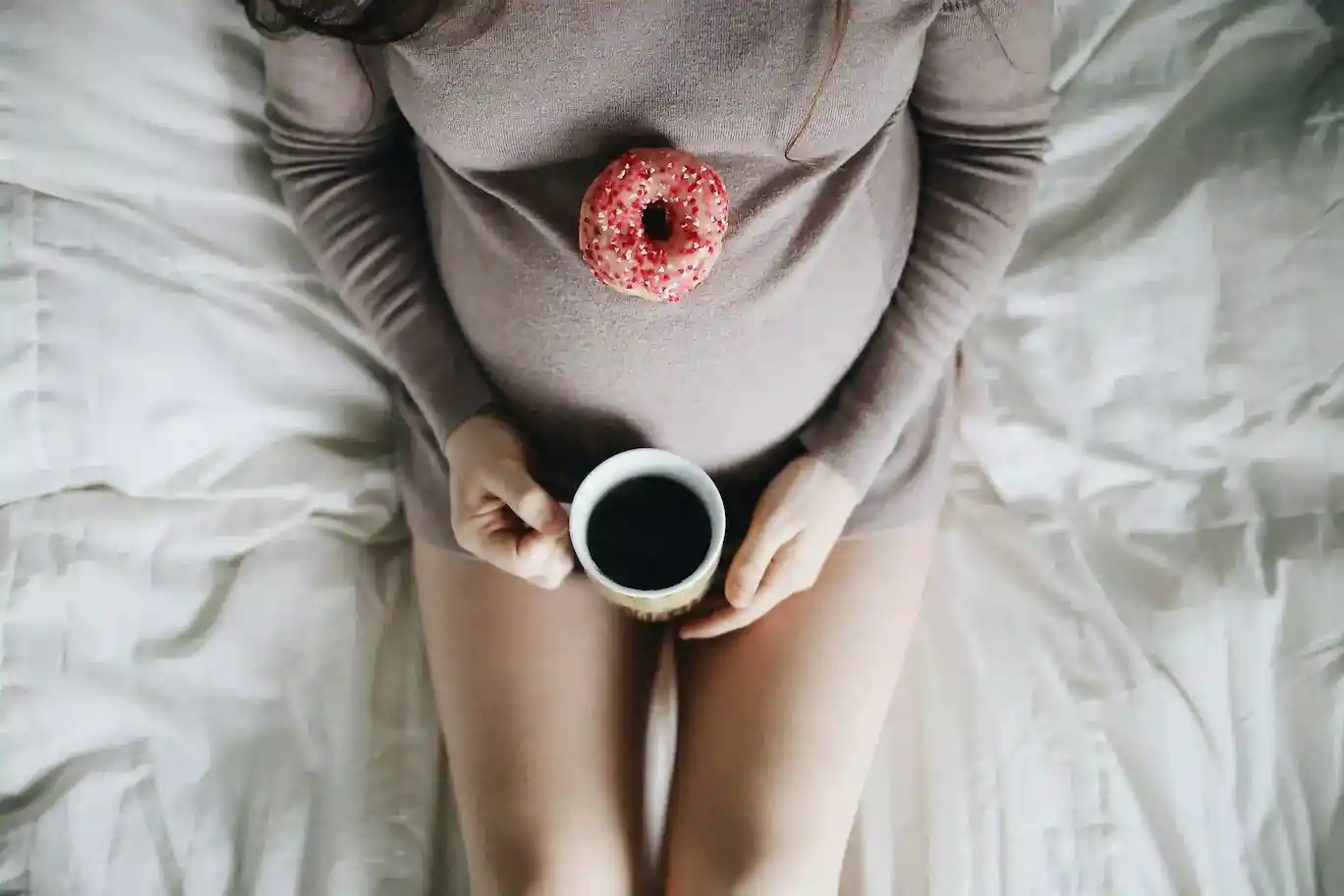 a pregnant woman holding a donut and a cup of coffee