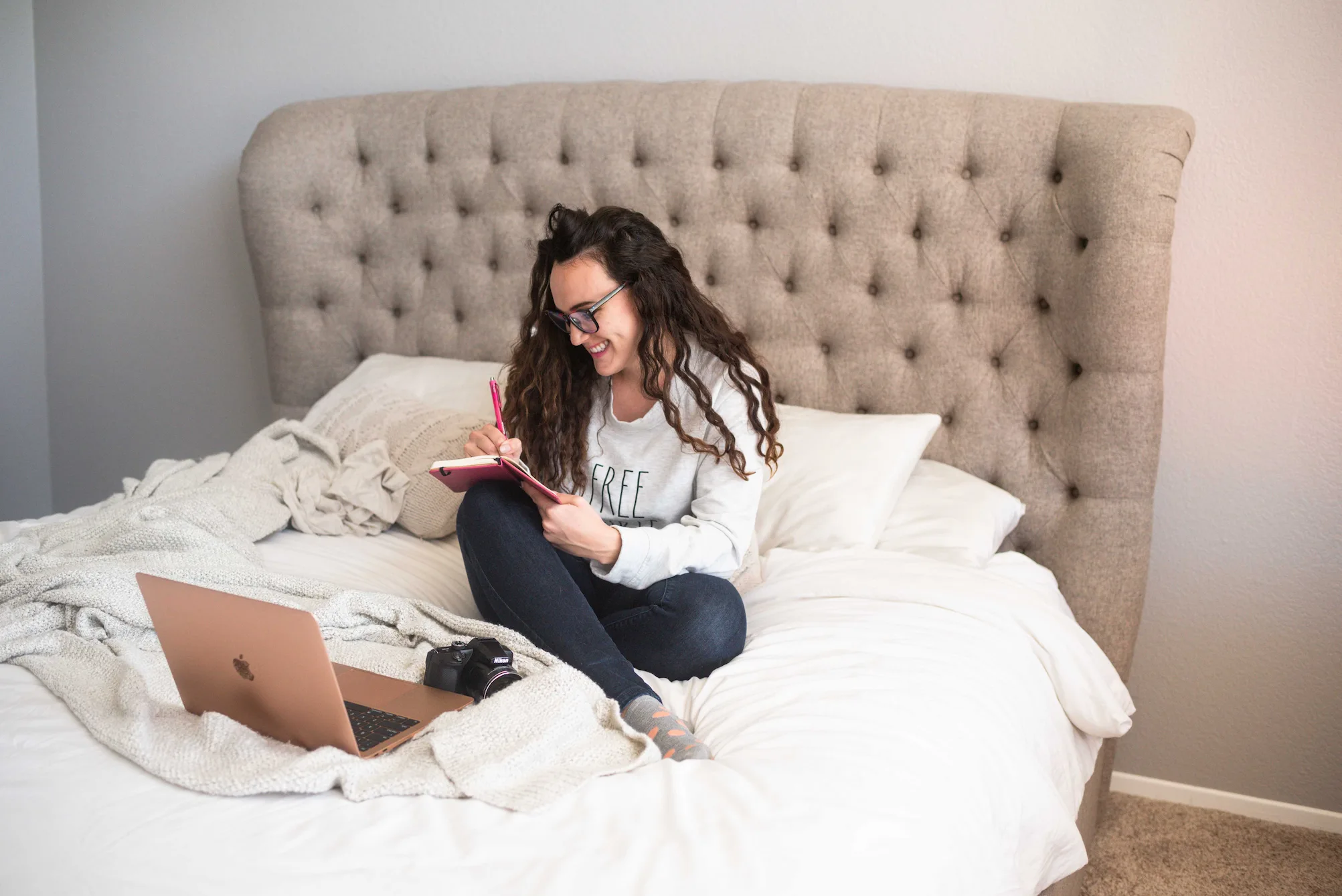 a woman sitting on a bed writing on a notebook