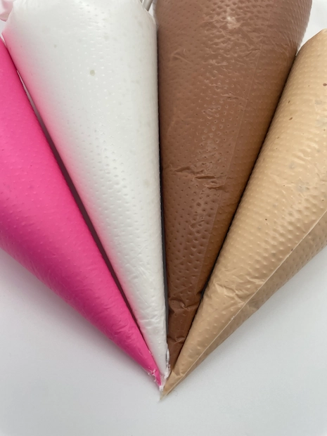 Piping bags filled with pink, white and brown royal icing